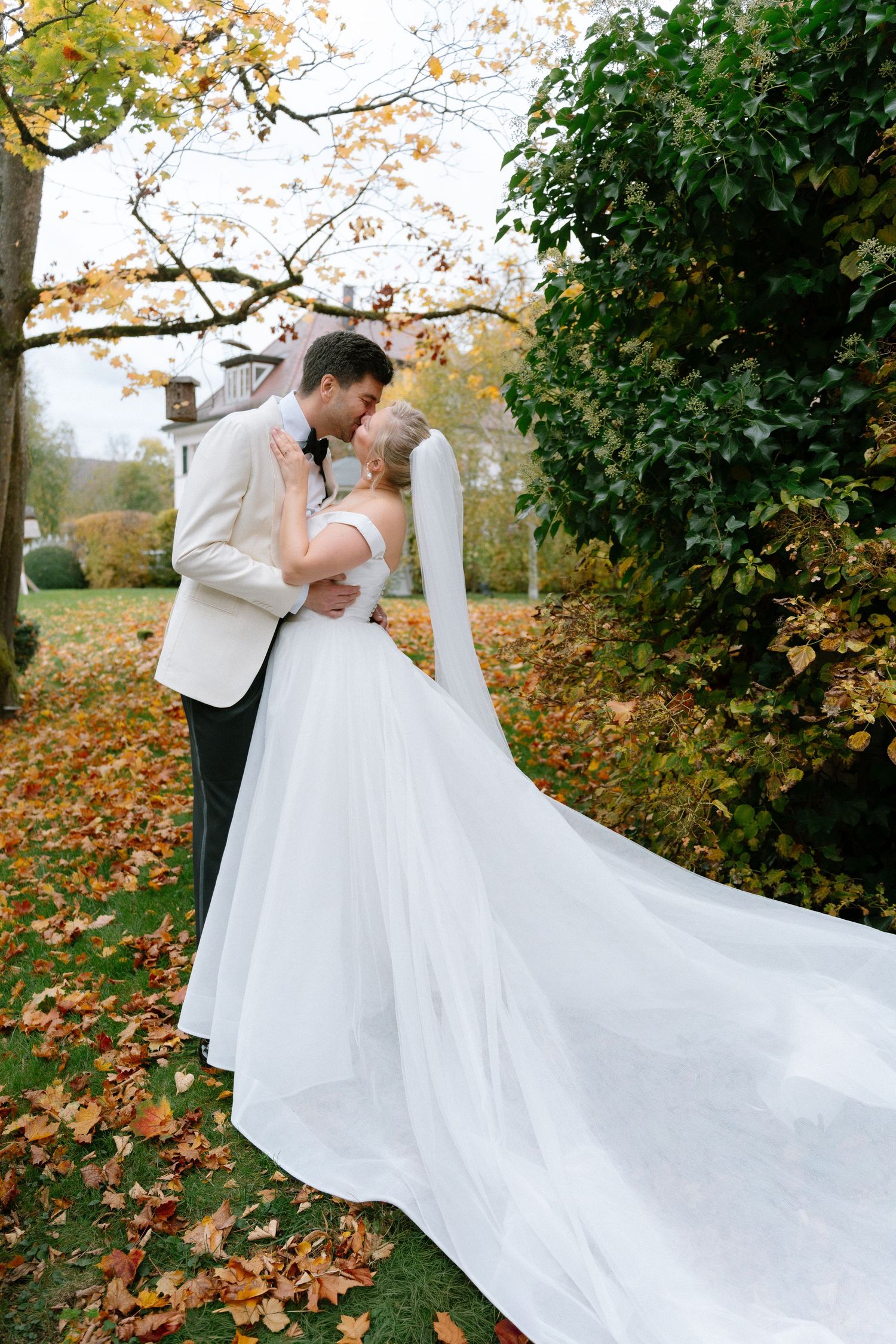 A romantic wedding couple embraces in an autumn garden with fallen leaves and a flowing white dress train.