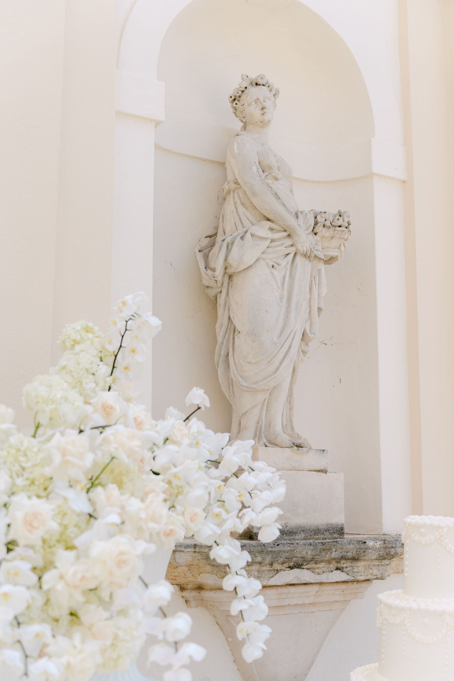 Classical white marble statue in an alcove with delicate white orchids and hydrangeas creating an elegant display. Villa Mosconi Bertani