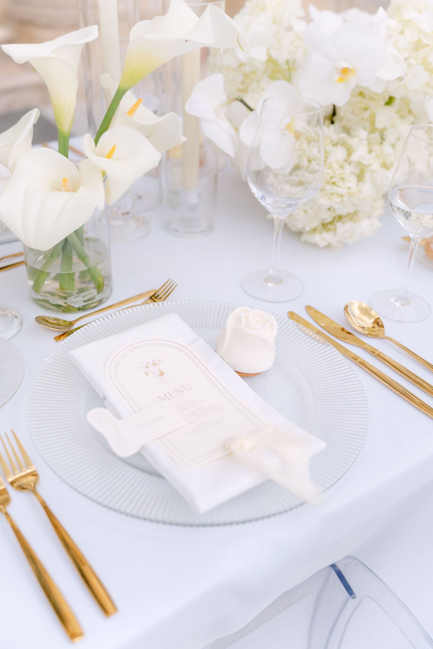 Elegant white and gold place settings with floral centerpieces create a sophisticated wedding table design. Villa Mosconi Bertani