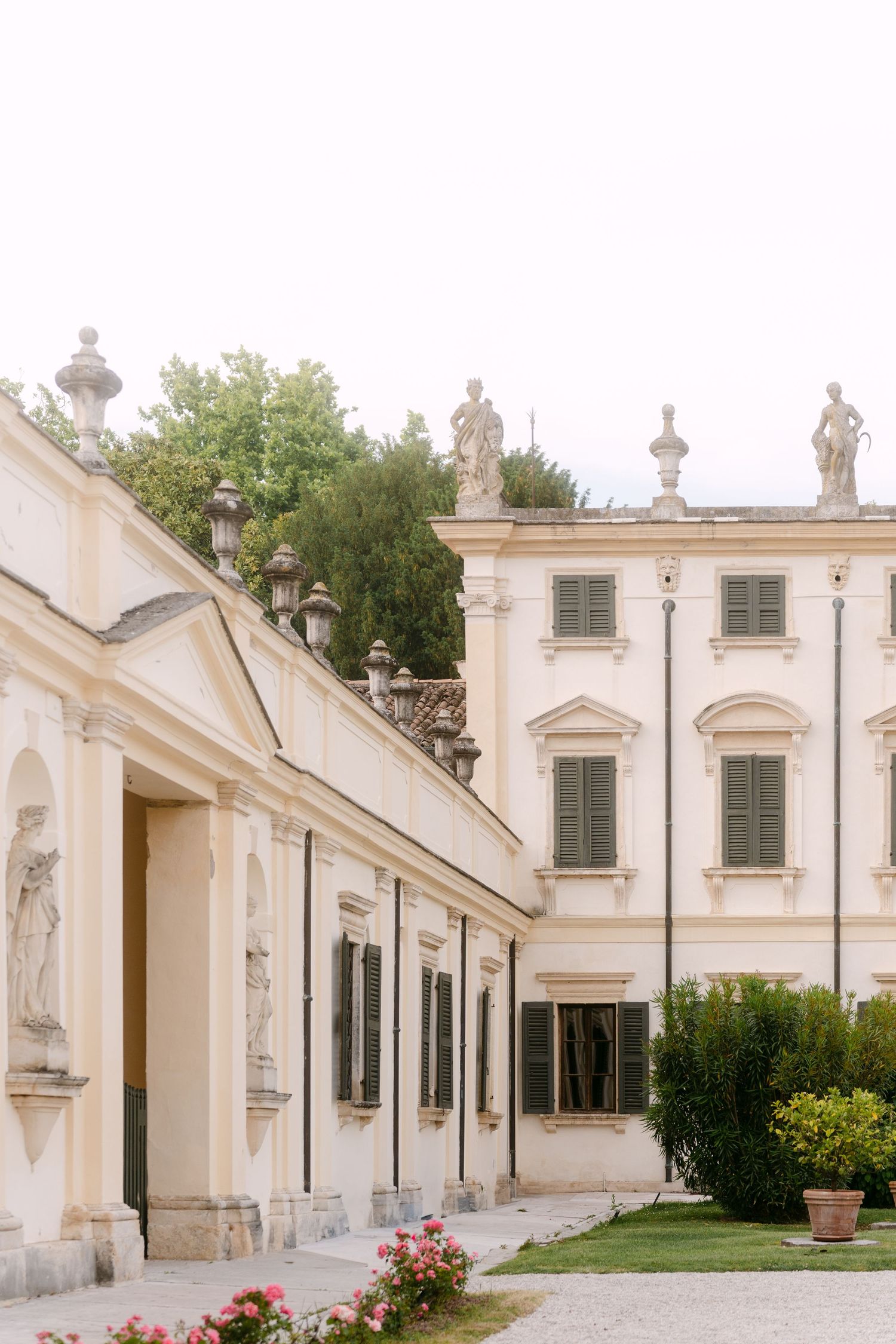 Elegant white neoclassical building facade with statues and rose gardens.