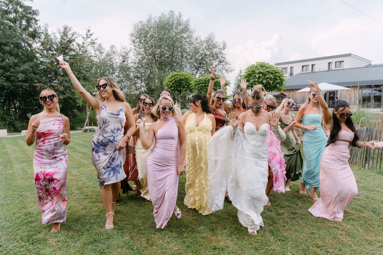 A group of people in floral and pink dresses running joyfully through a grassy field during a summer celebration.
