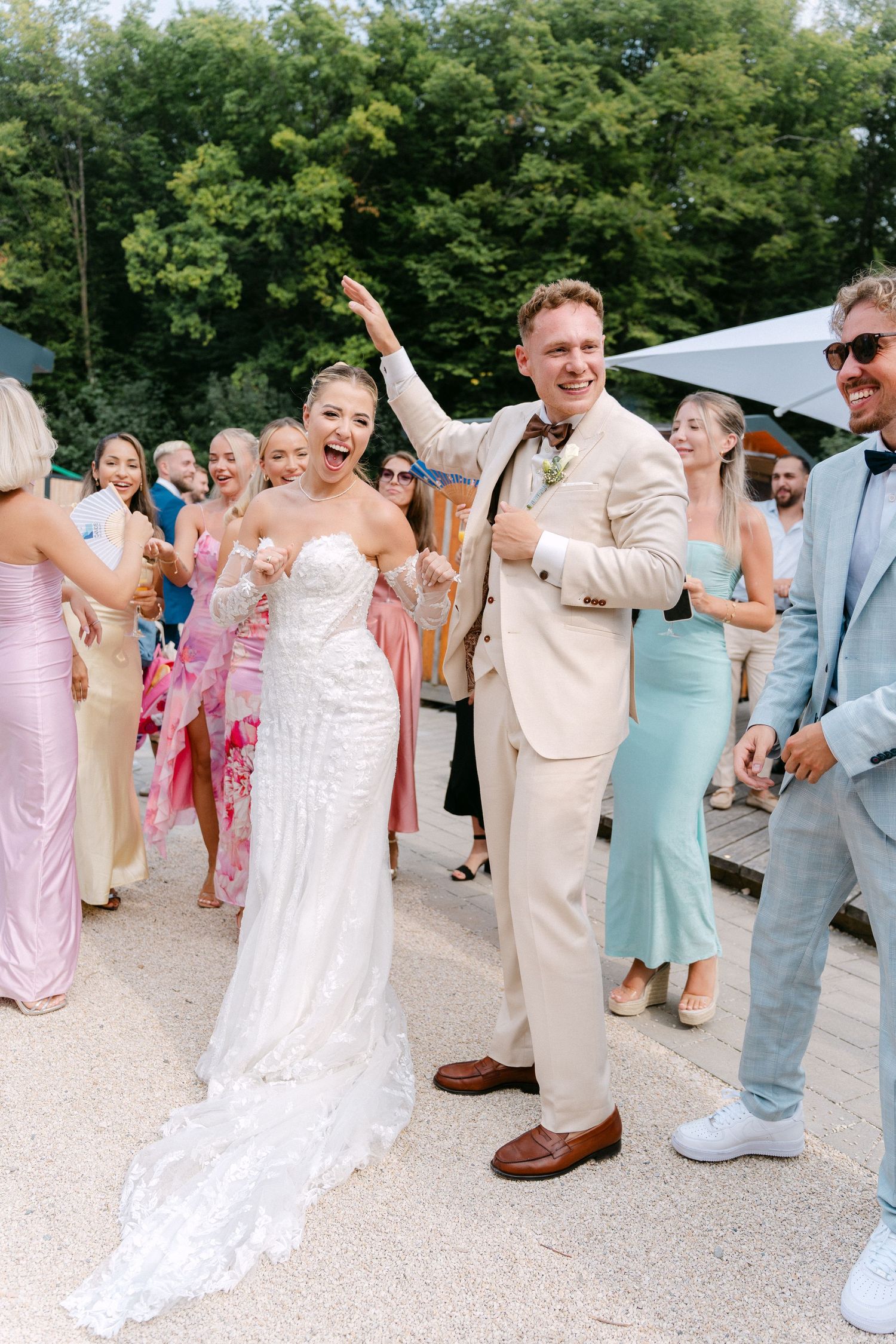 Wedding party dances and celebrates together outdoors in pastel attire at a summer celebration.