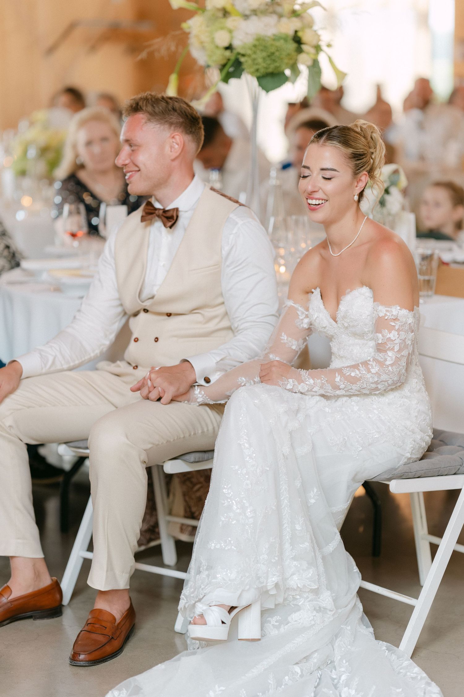 A couple shares a joyful moment during their wedding reception, with the bride wearing a long-sleeved lace gown.