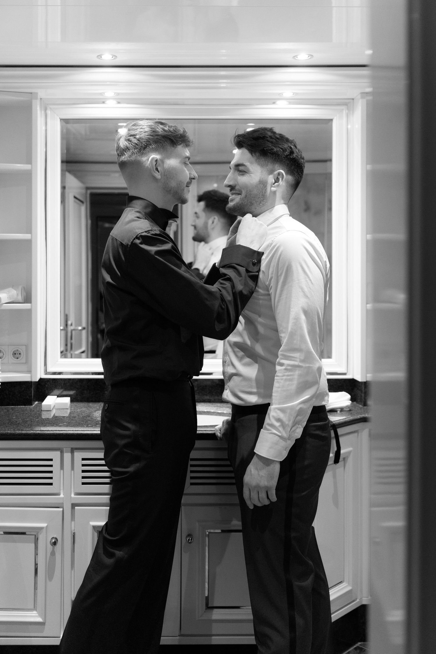 Two people having an intimate moment while standing in a kitchen, captured in black and white.