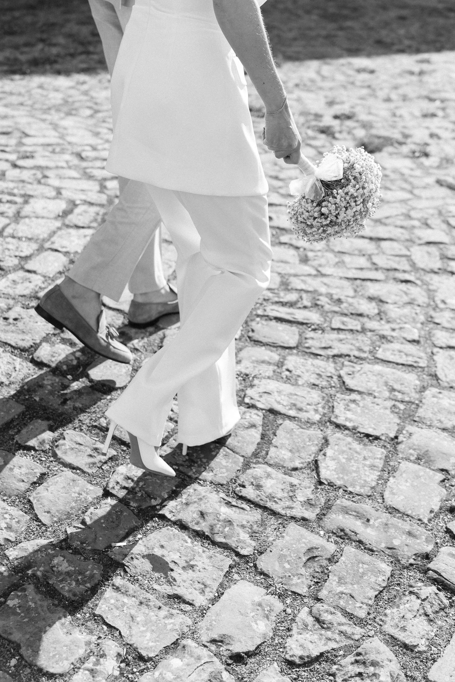 Black and white image of feet walking on cobblestone pavement in white clothing. Schloss Solitude