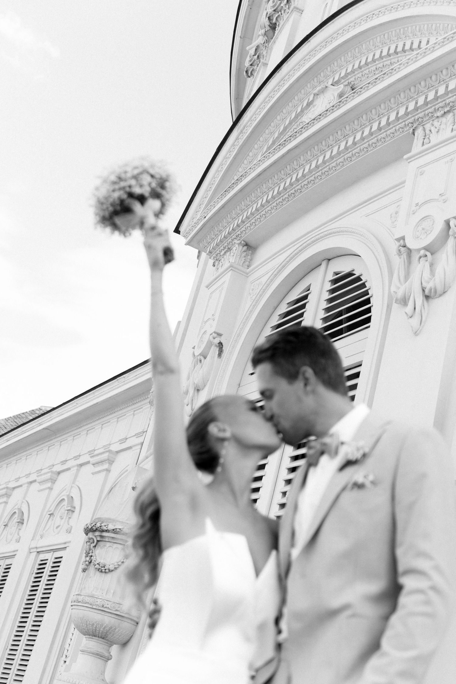 A romantic black and white wedding photo showing a couple sharing a kiss in front of an ornate classical building. Schloss Solitude