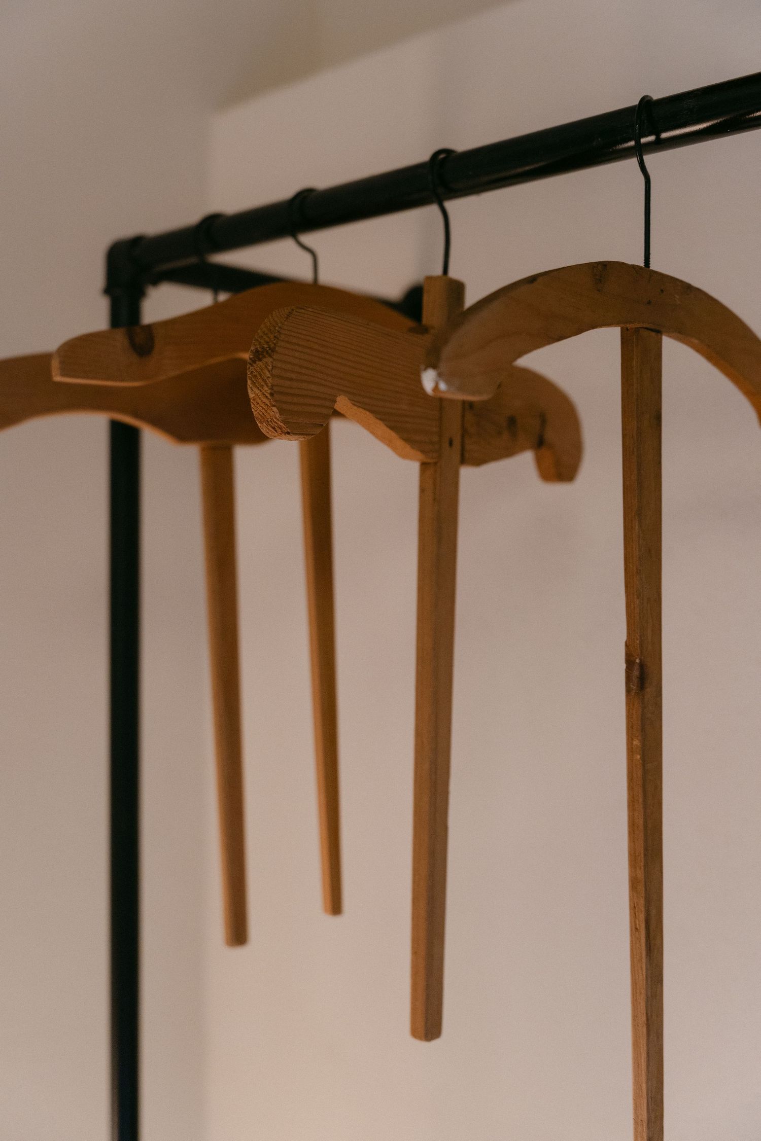 Row of wooden coat hangers mounted on a dark rail against a white wall.