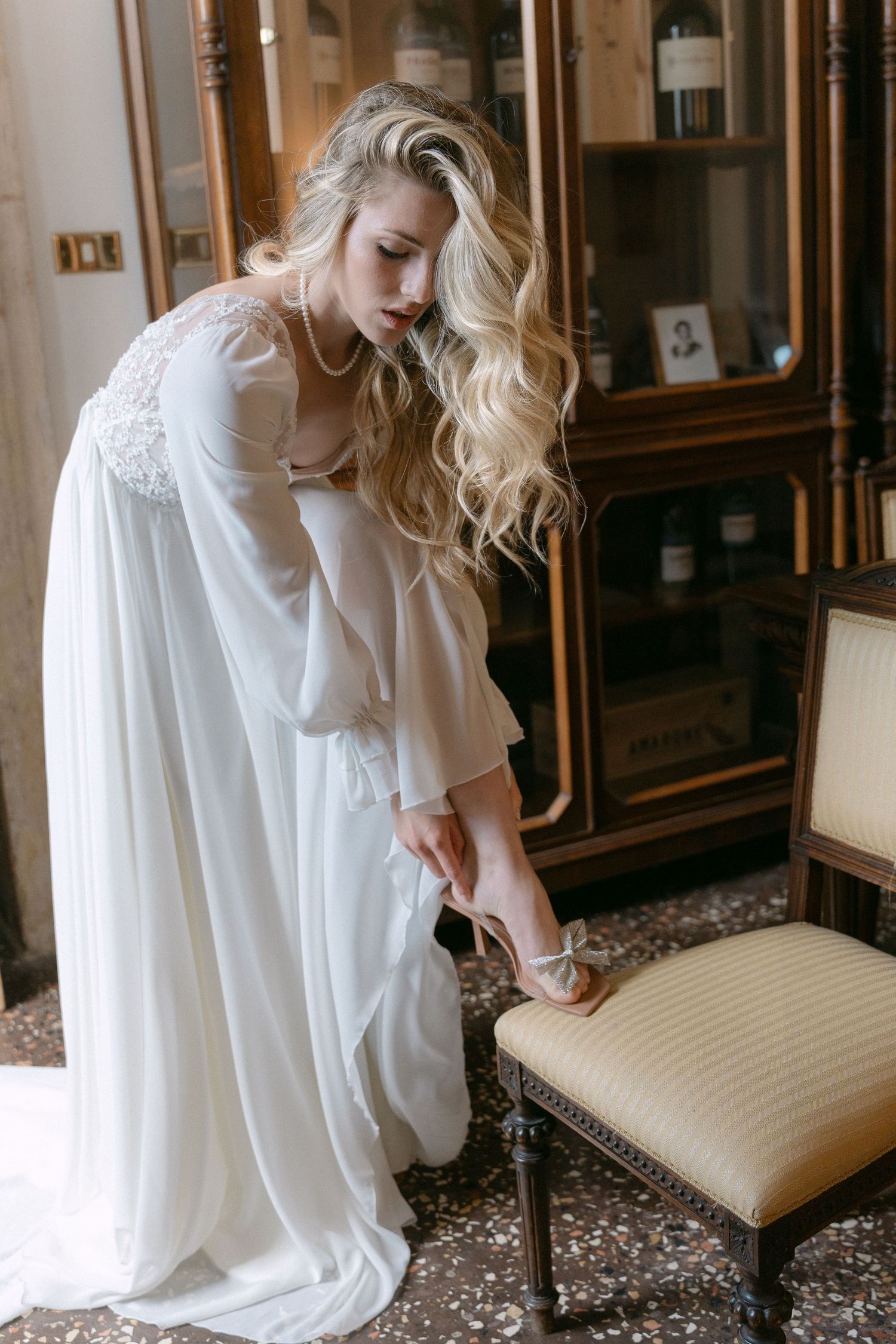 Interior scene with vintage furniture and flowing white dress in soft lighting.