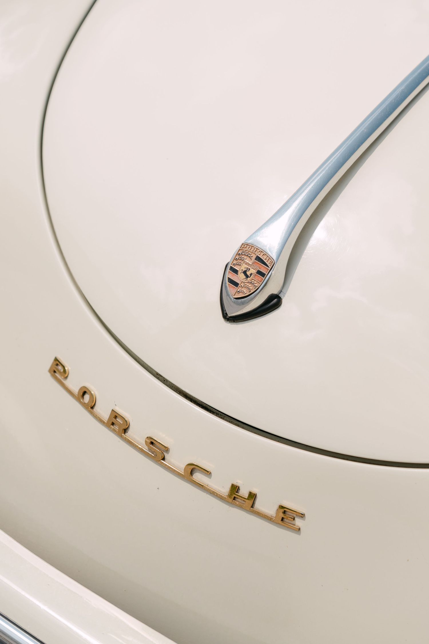 Close-up view of a vintage Porsche hood emblem and lettering on a cream colored classic car. Villa Mosconi Bertani