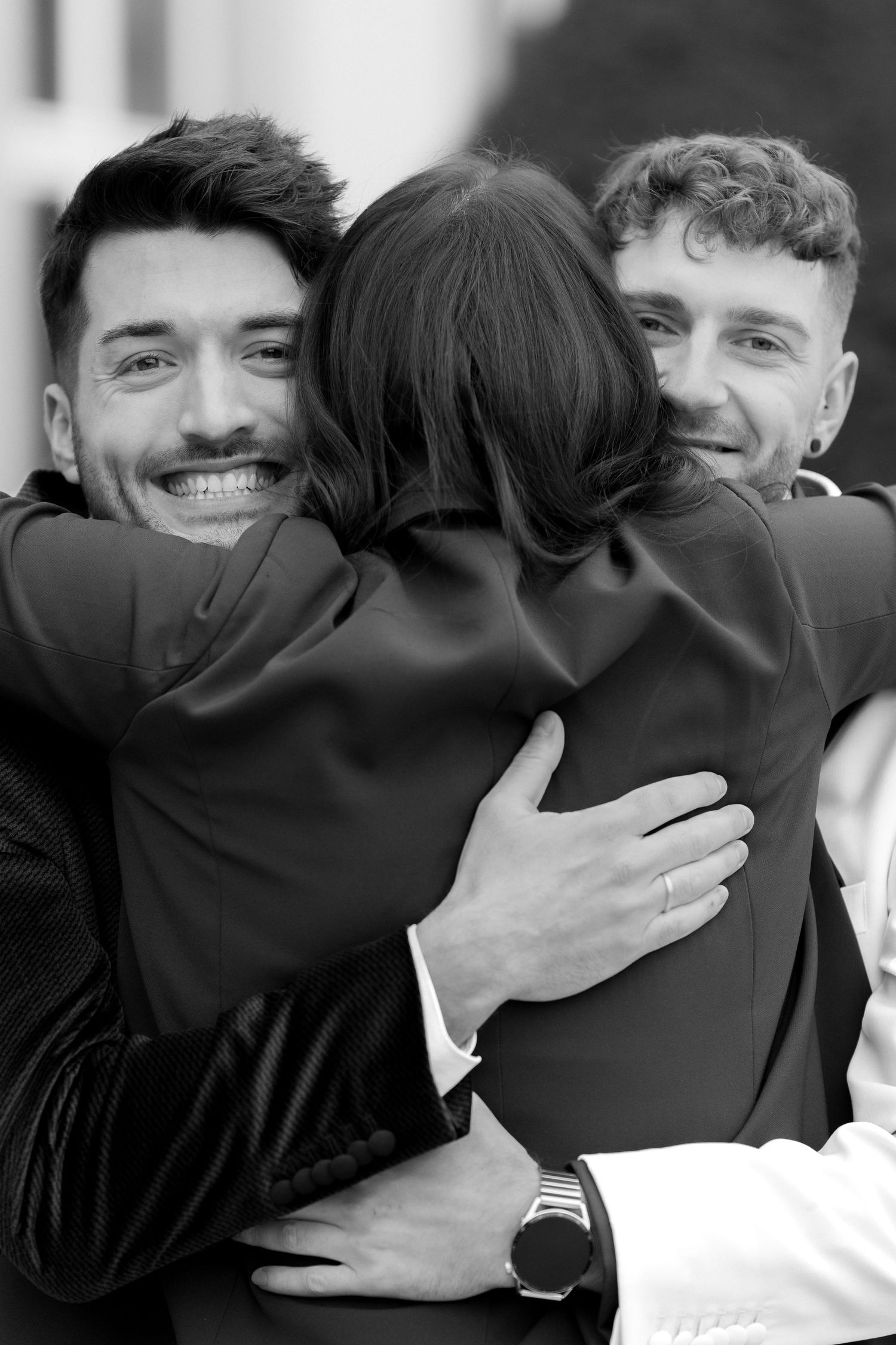 A candid black and white photo showing three people in a warm embrace, smiling and hugging.