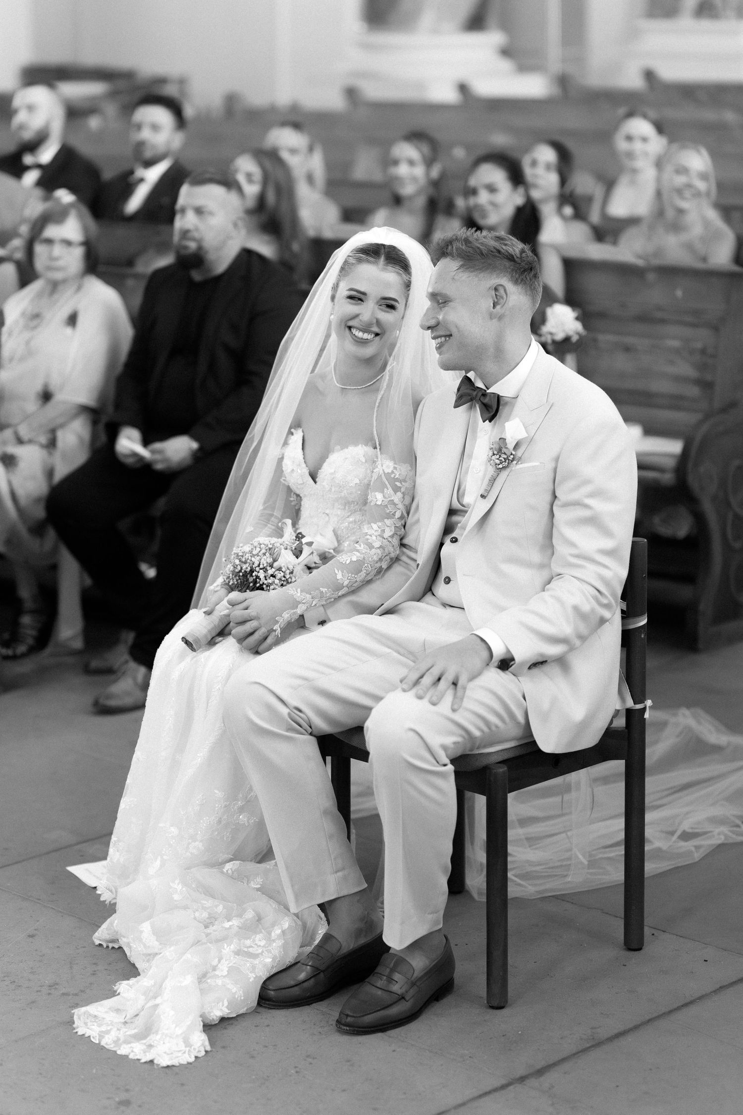 A bride and groom share a joyful moment while sitting together at their wedding ceremony.