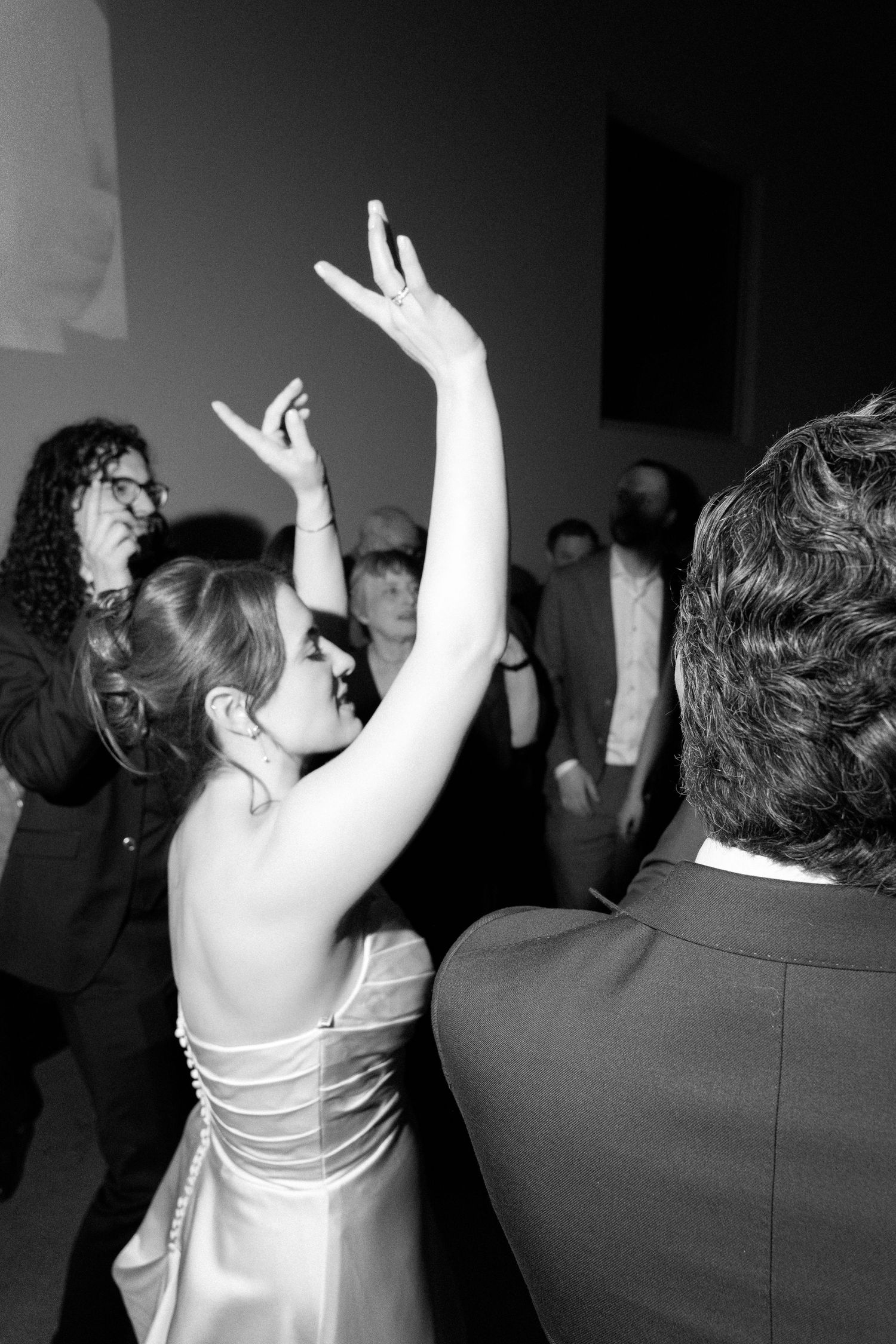 A woman in a satin dress raises her arm while dancing at a formal event in this black and white photo.