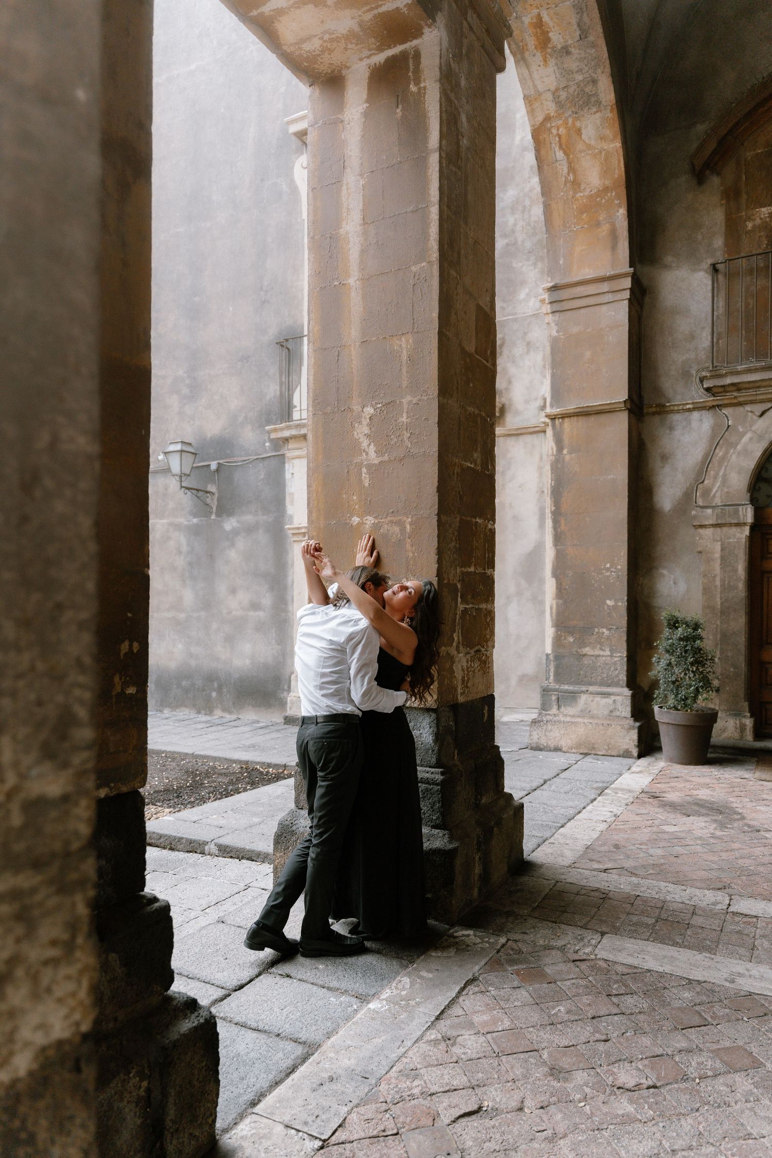 Couple dancing romantically under stone arches in an ancient courtyard, bathed in soft natural light.