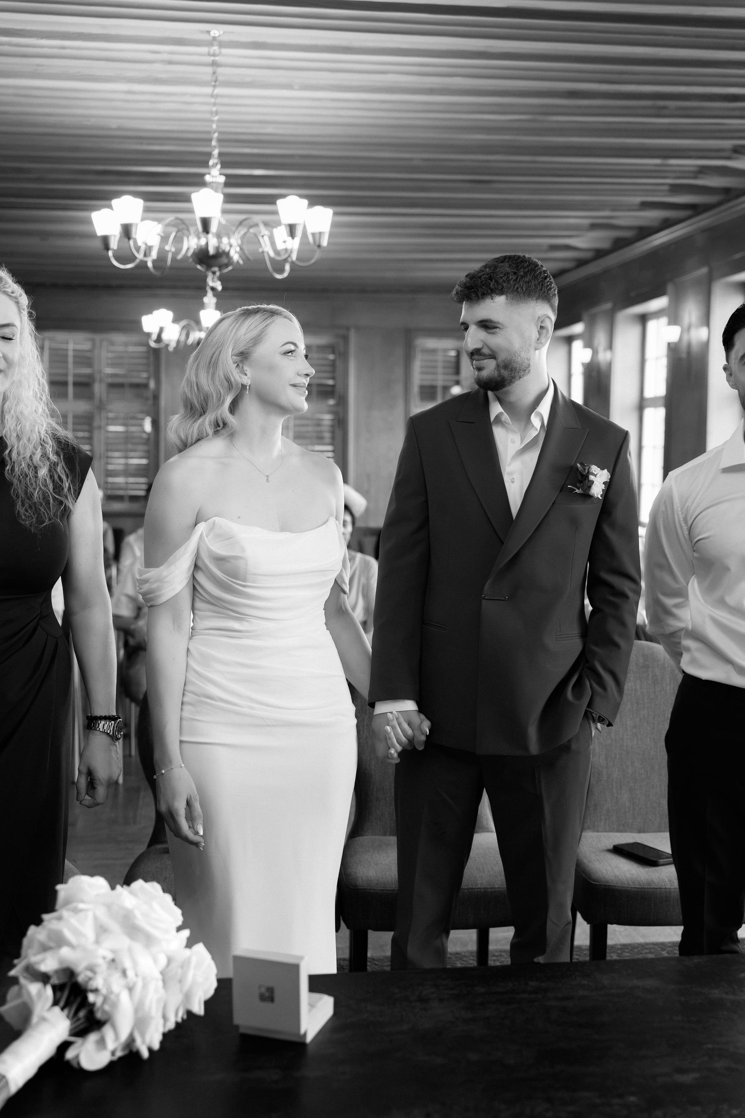 Black and white photo of a bride and groom holding hands at their wedding ceremony indoors.
