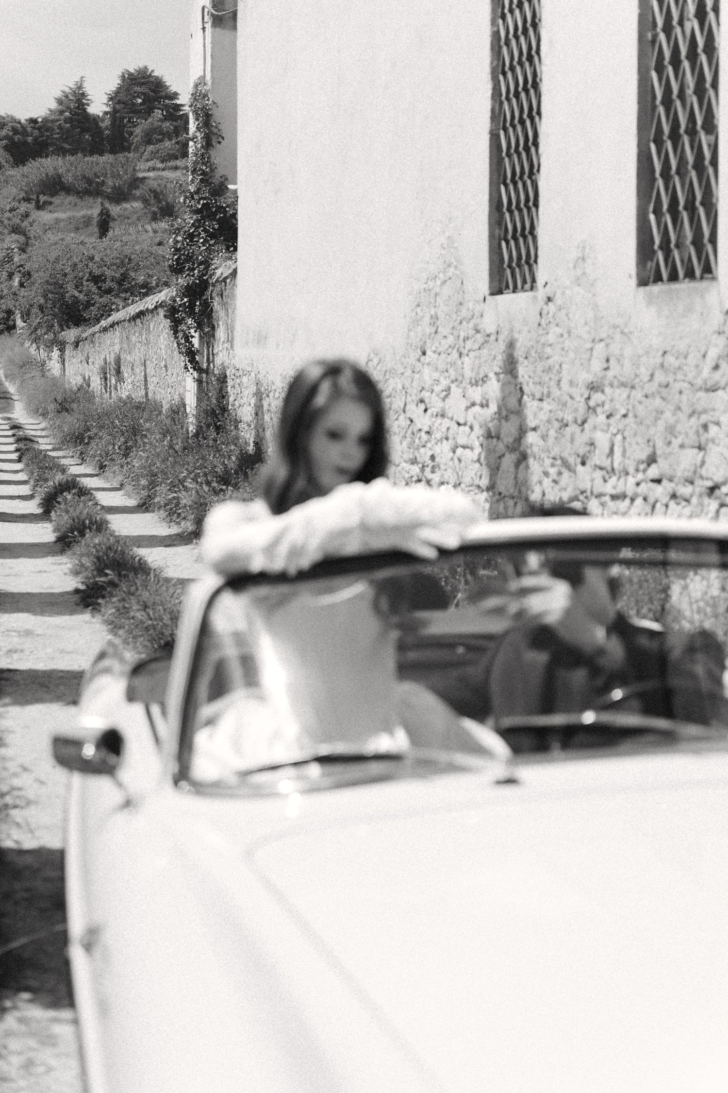 A vintage car decorated for a wedding sits parked outside a stone building with arched windows.