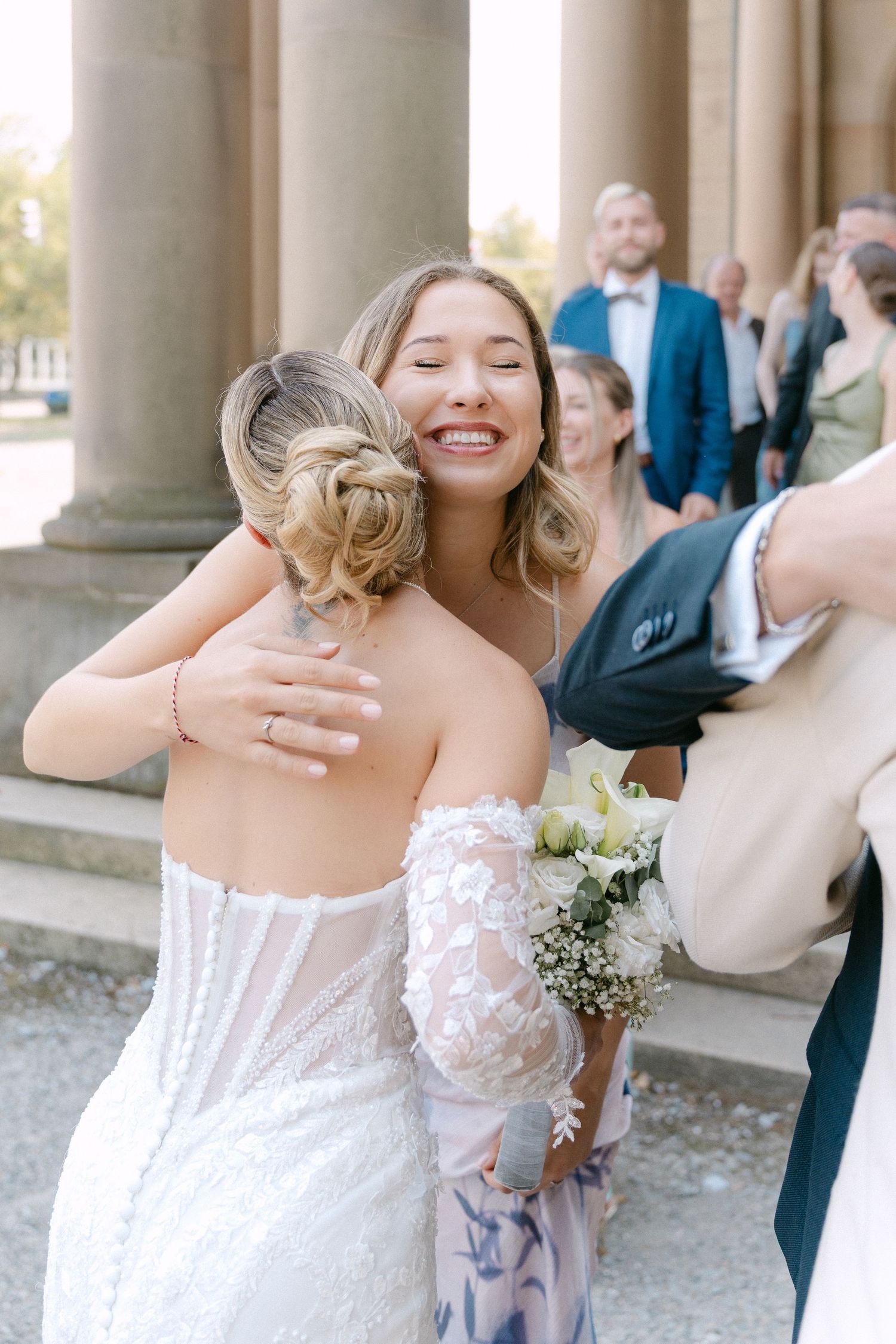 A bride in a white lace wedding dress smiles and dances with joy during an outdoor wedding celebration.