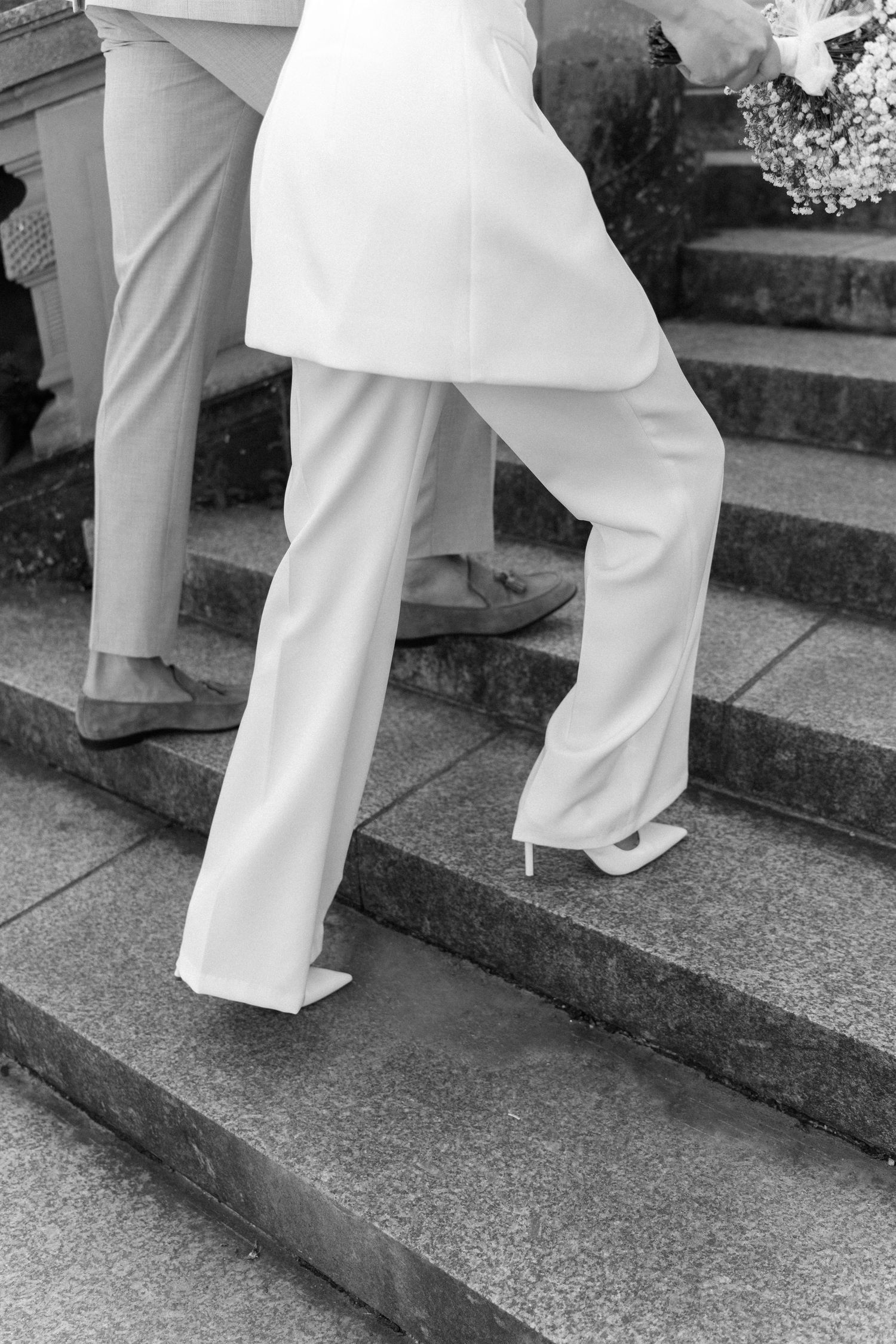 Black and white photo of legs in white formal pants walking up stone steps at a wedding. Schloss Solitude