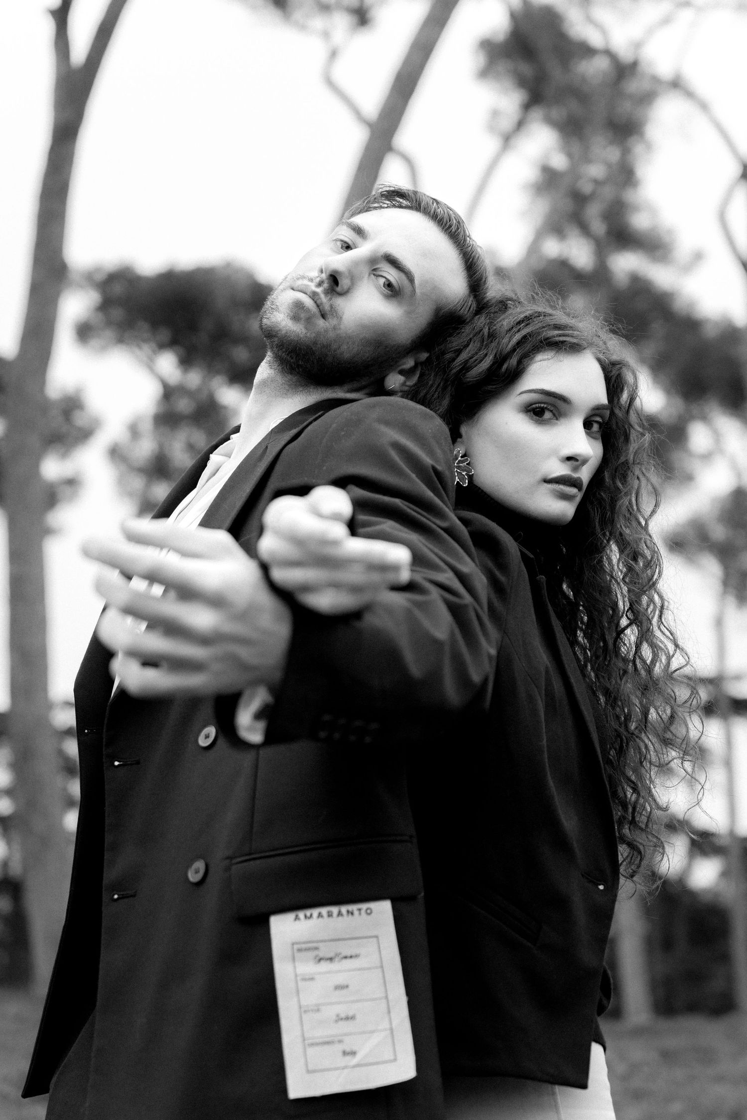 Dramatic black and white portrait of a couple in dark clothing posing back-to-back outdoors.