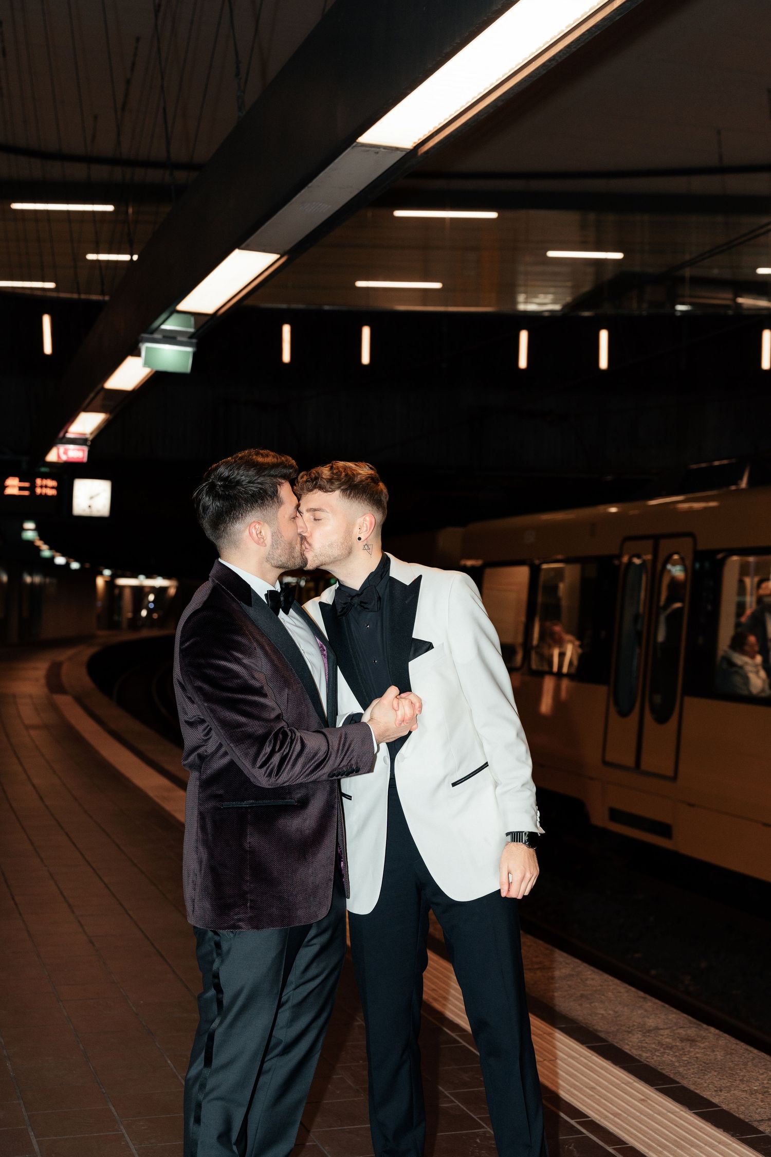Two people in formal attire share a romantic moment at a subway station platform at night.