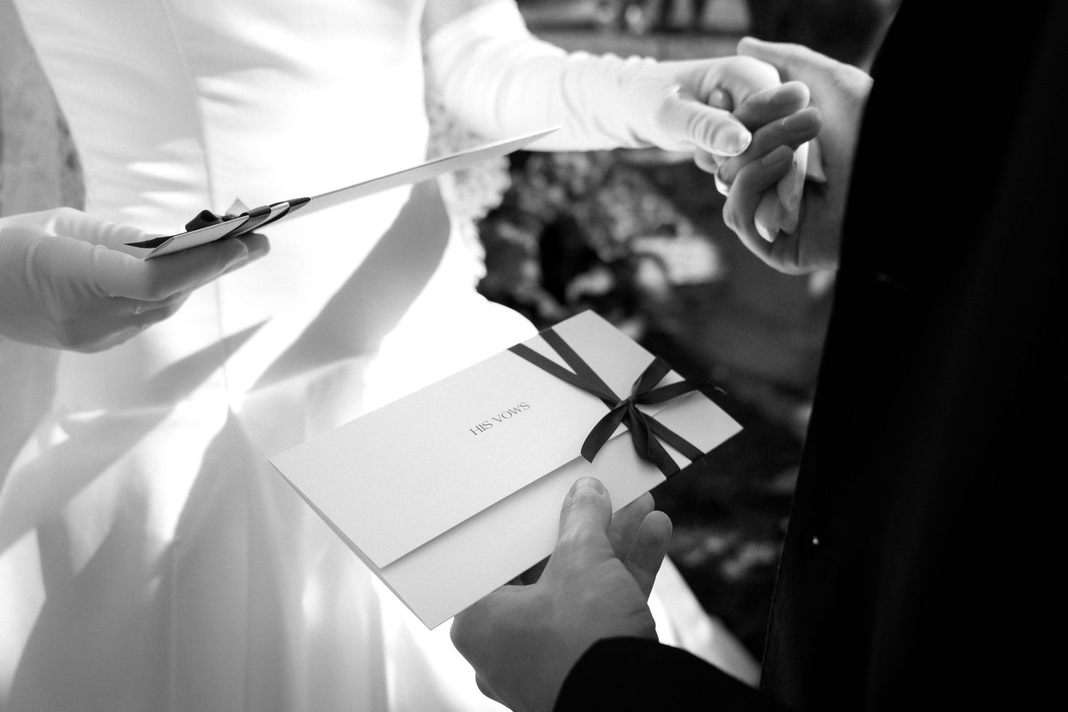 Black and white photo of a bride and groom exchanging wedding vows booklets during an outdoor ceremony.