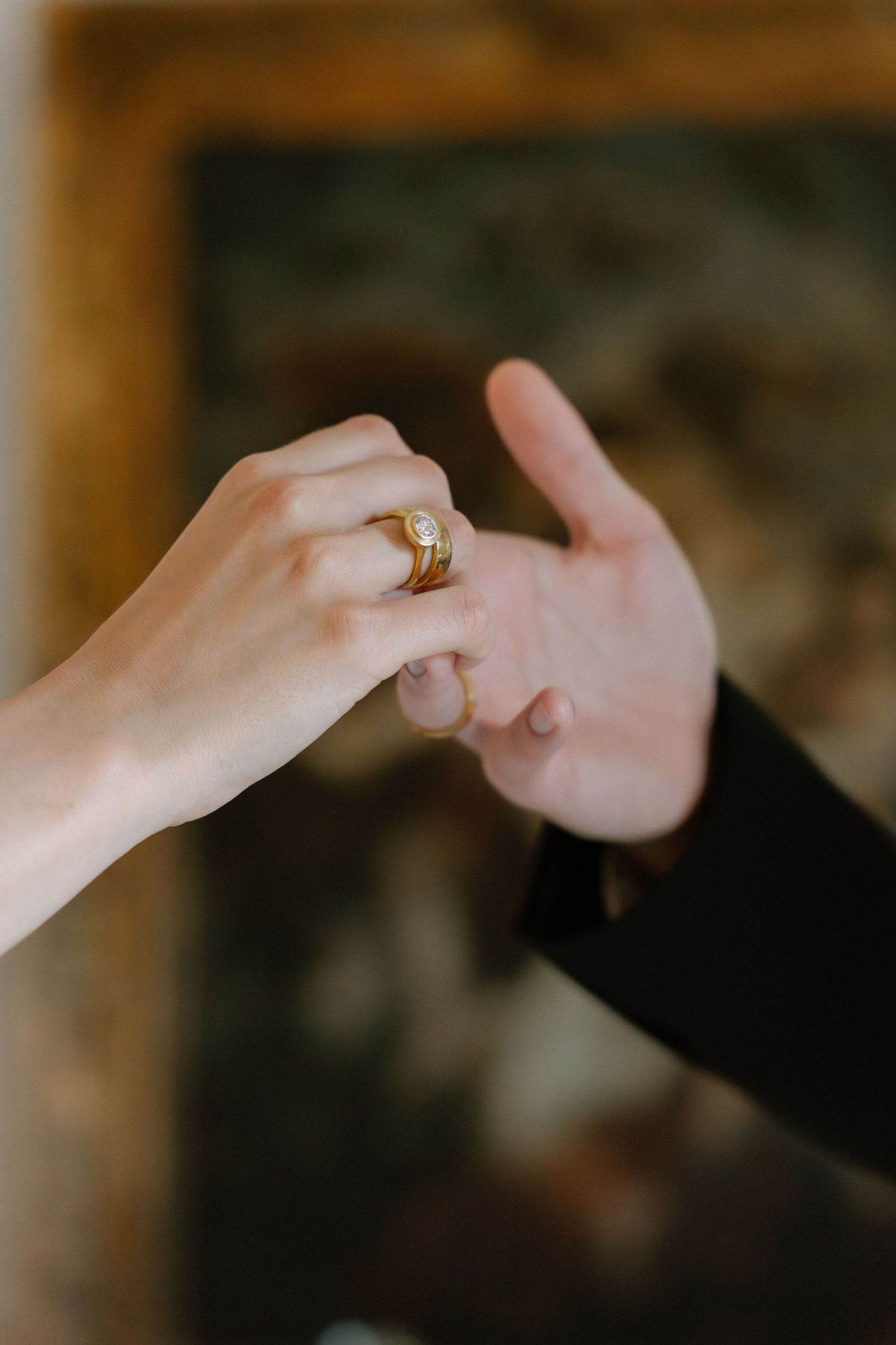 Two hands touching with a gold diamond engagement ring on the woman's finger.