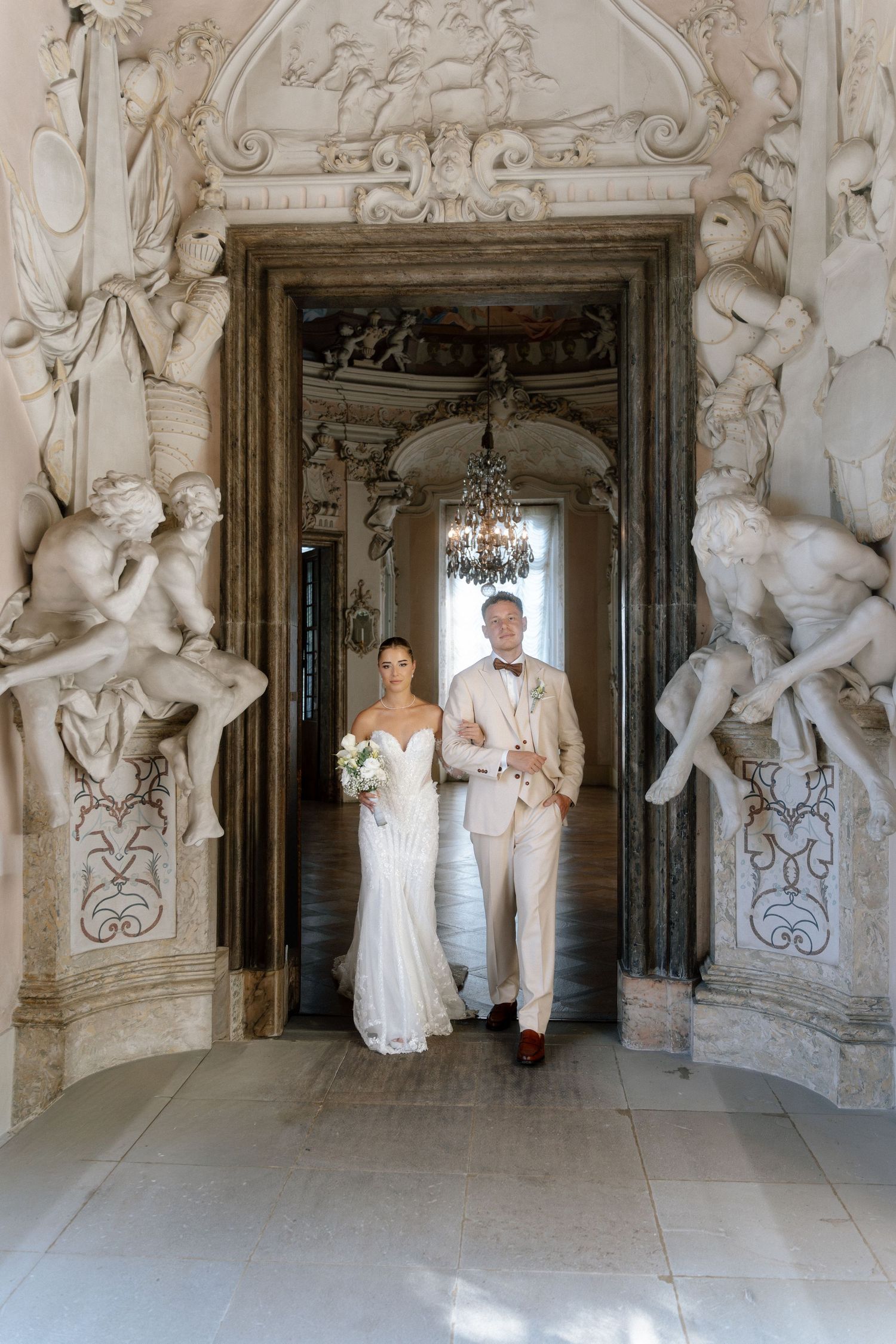 Elegant wedding party poses in a grand baroque hallway adorned with ornate white sculptures and architectural details. Schloss Ludwigsburg