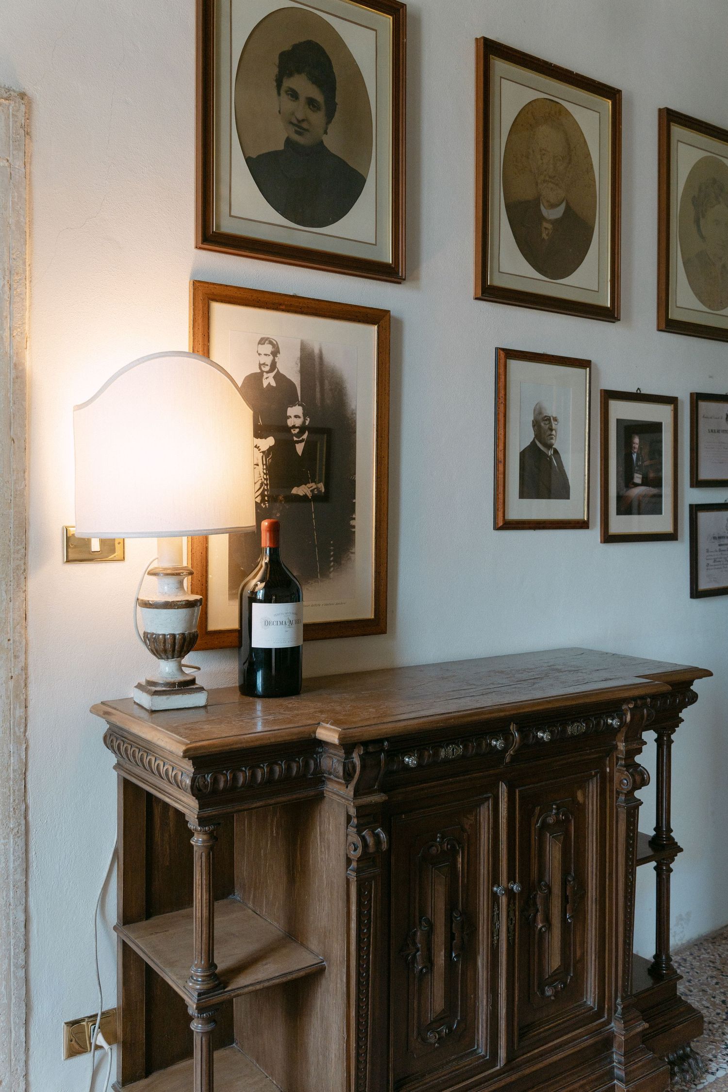 A hallway with vintage framed portraits on white walls and antique wooden furniture with table lamps. Wedding Verona