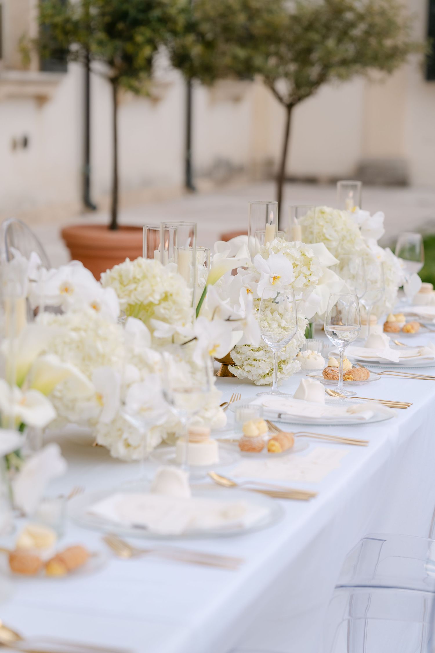 Elegant white wedding table setting with hydrangeas and peonies in a minimalist outdoor setting with peach accents. Villa Mosconi Bertani