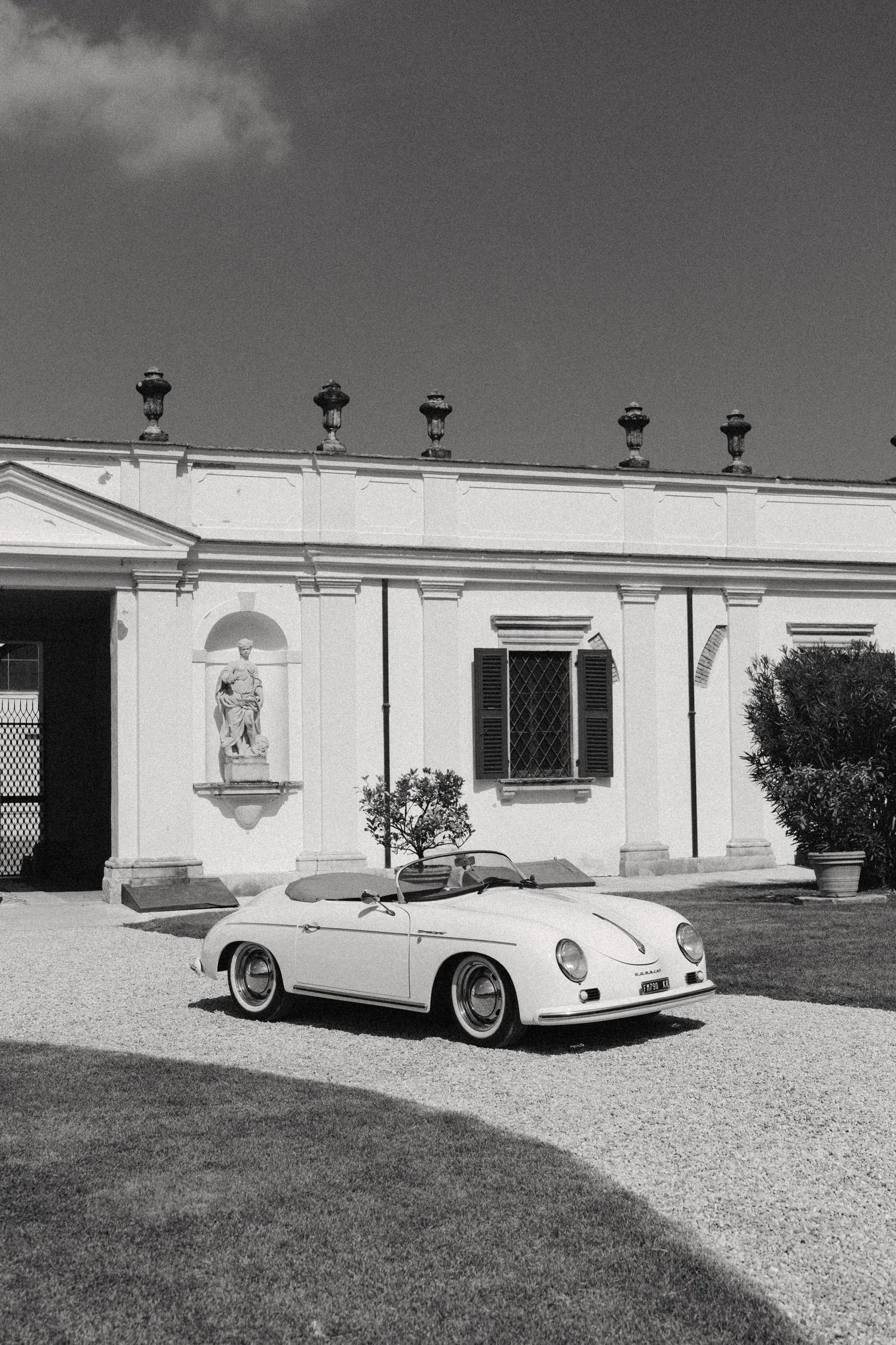 A classic Porsche 356 automobile parked in front of a white modernist building in black and white photography. Villa Mosconi Bertani
