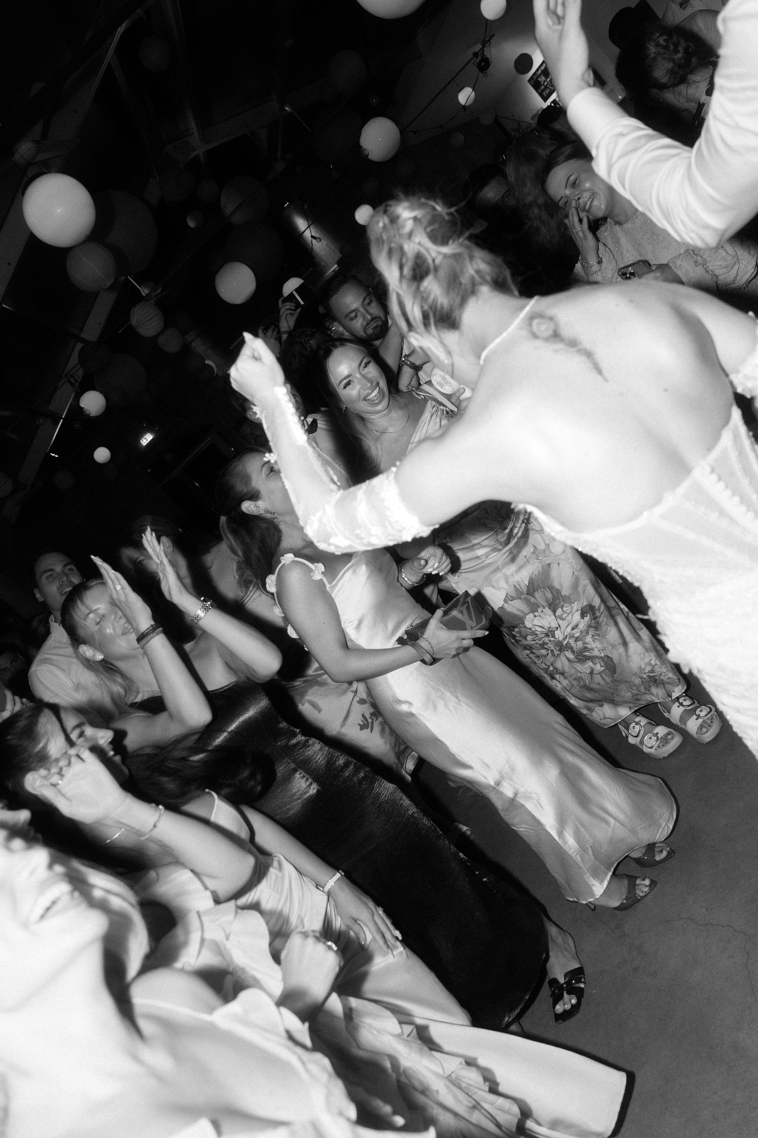 Black and white photo showing people dancing and celebrating at a lively party or nightclub event.