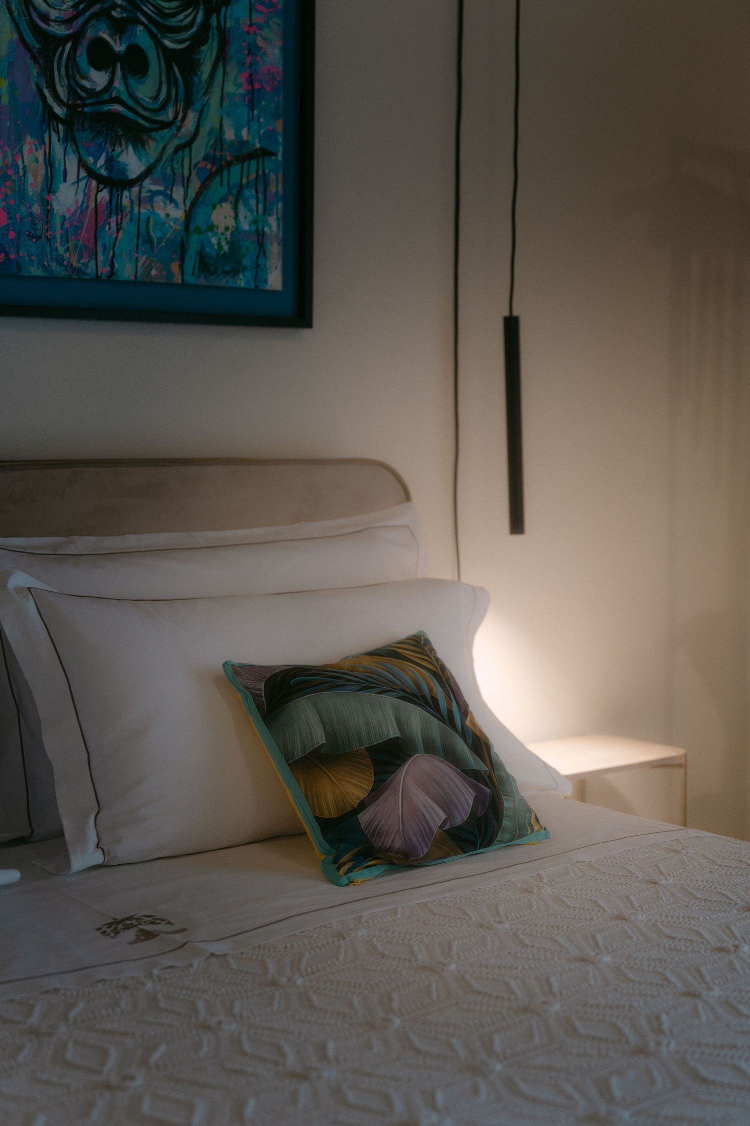 A modern bedroom interior with a white bed and colorful artwork on the wall.
