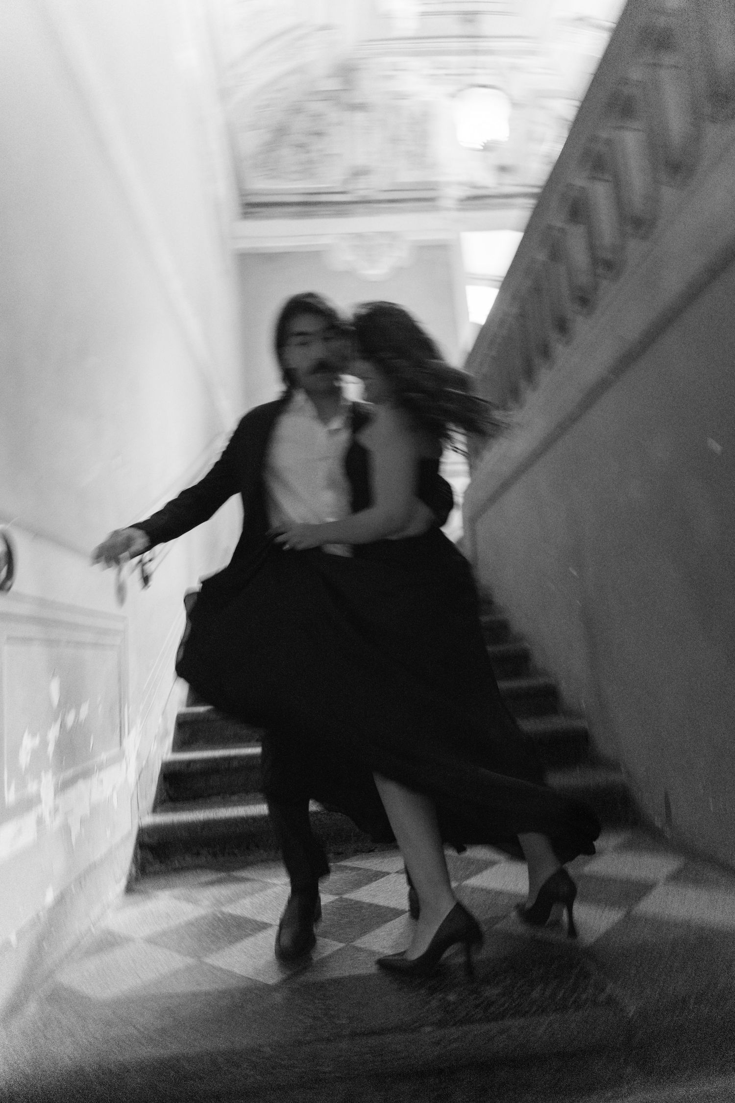 Black and white photo of a couple dancing passionately on grand staircase, motion blur capturing elegant movement.