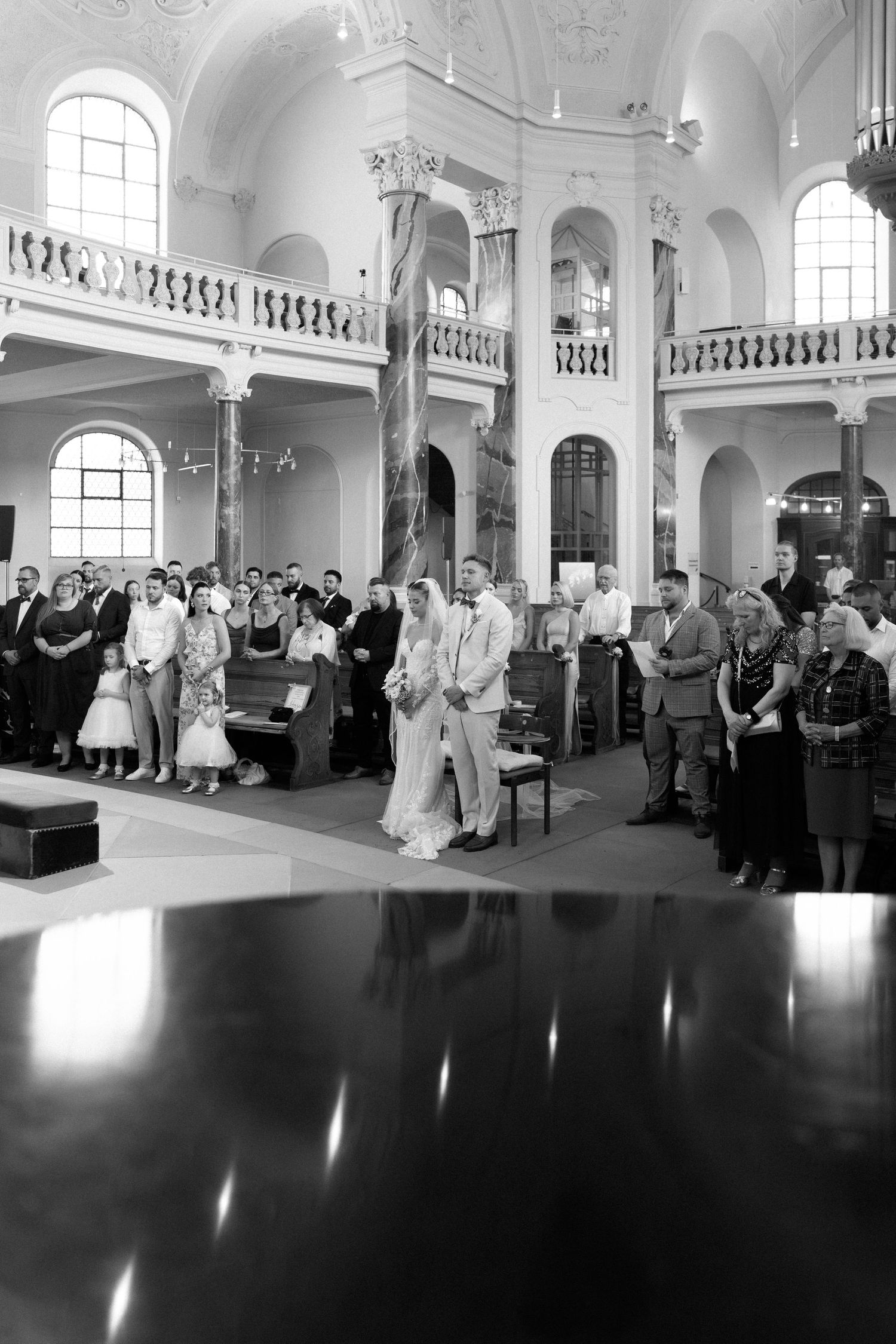 Black and white panoramic sequence of a wedding ceremony in an elegant historic ballroom with ornate architectural details.