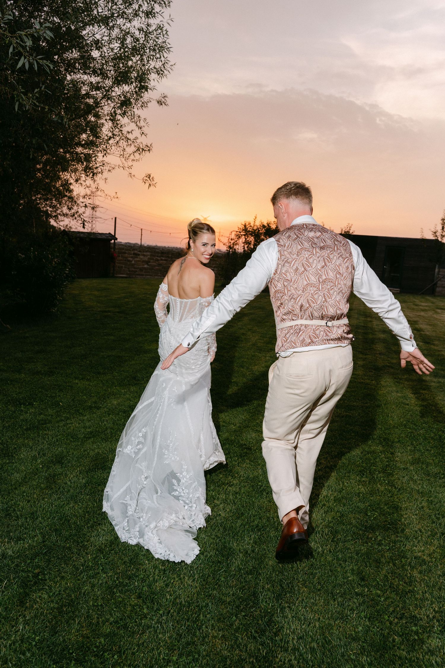 A couple in wedding attire dances playfully in a grassy field at sunset, creating a series of silhouetted poses.