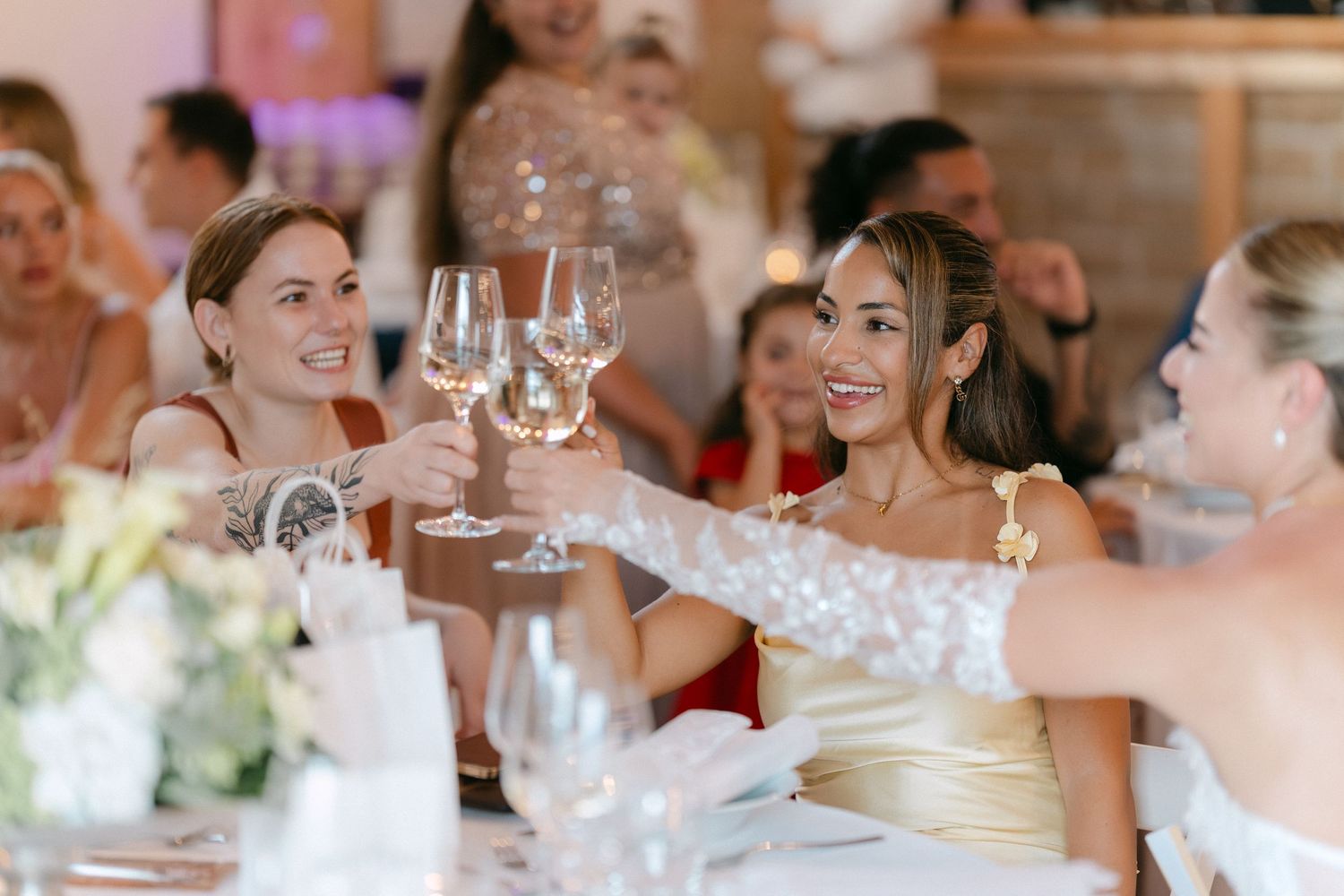 Wedding guests raise their glasses in a celebratory toast at an elegant reception with soft lighting and wine glasses.