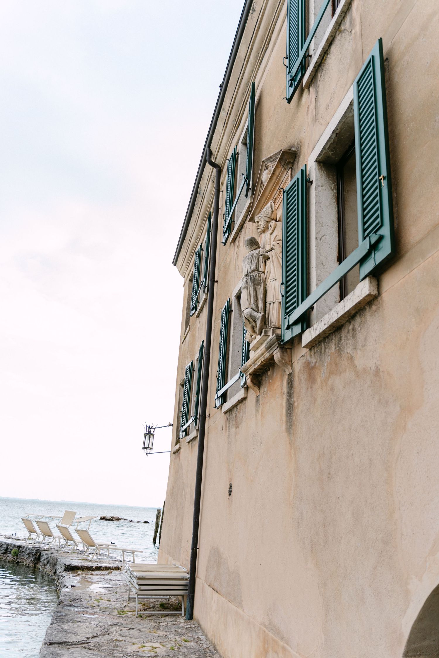 Green shuttered windows adorn a beige Mediterranean building facade with weathered walls and architectural details.