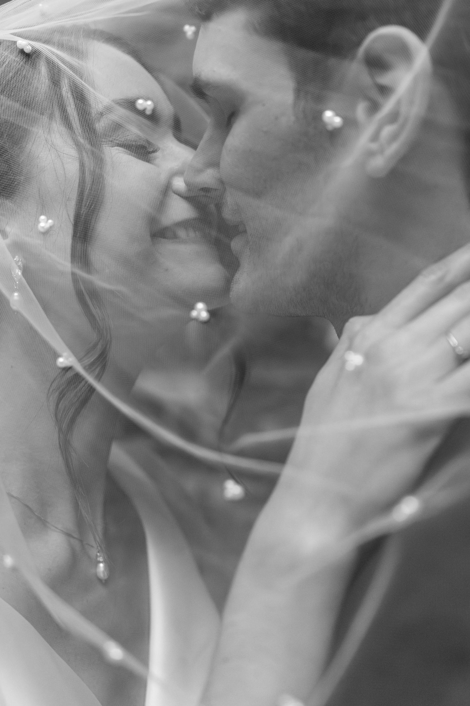 A romantic black and white wedding photo showing a tender moment under a veil with soft heart decorations.