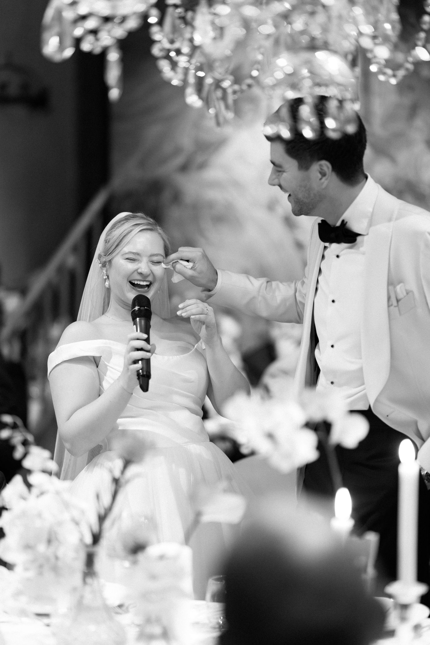 Intimate wedding reception moment captured under sparkling crystal chandeliers.