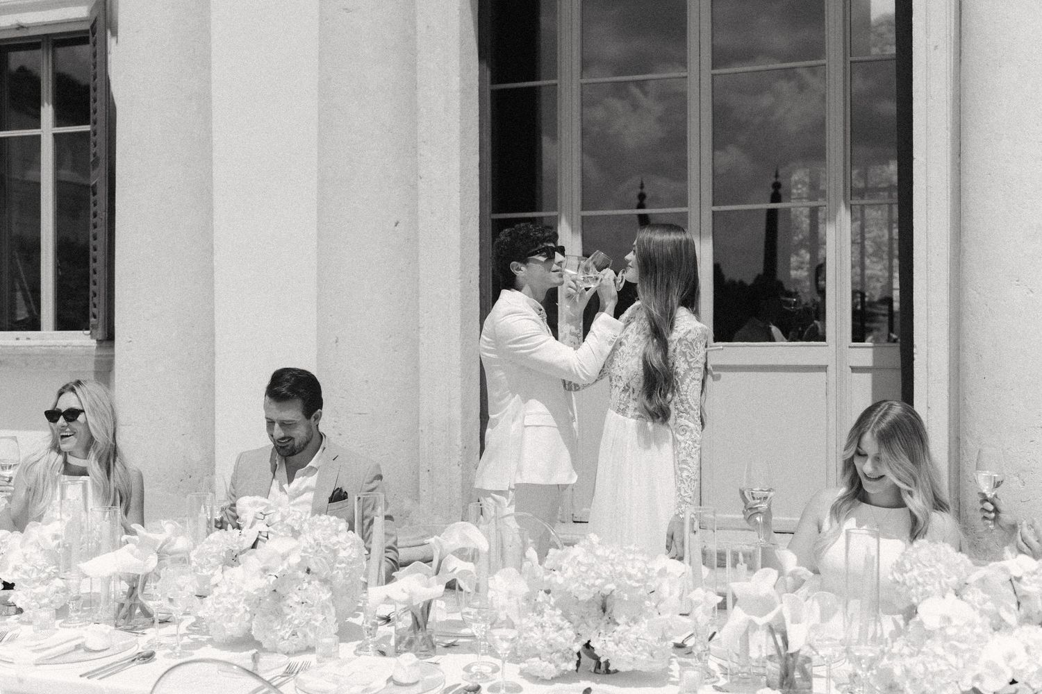 A large group of people sit at a formal banquet table with white tablecloths and elegant place settings. Villa Mosconi Bertani