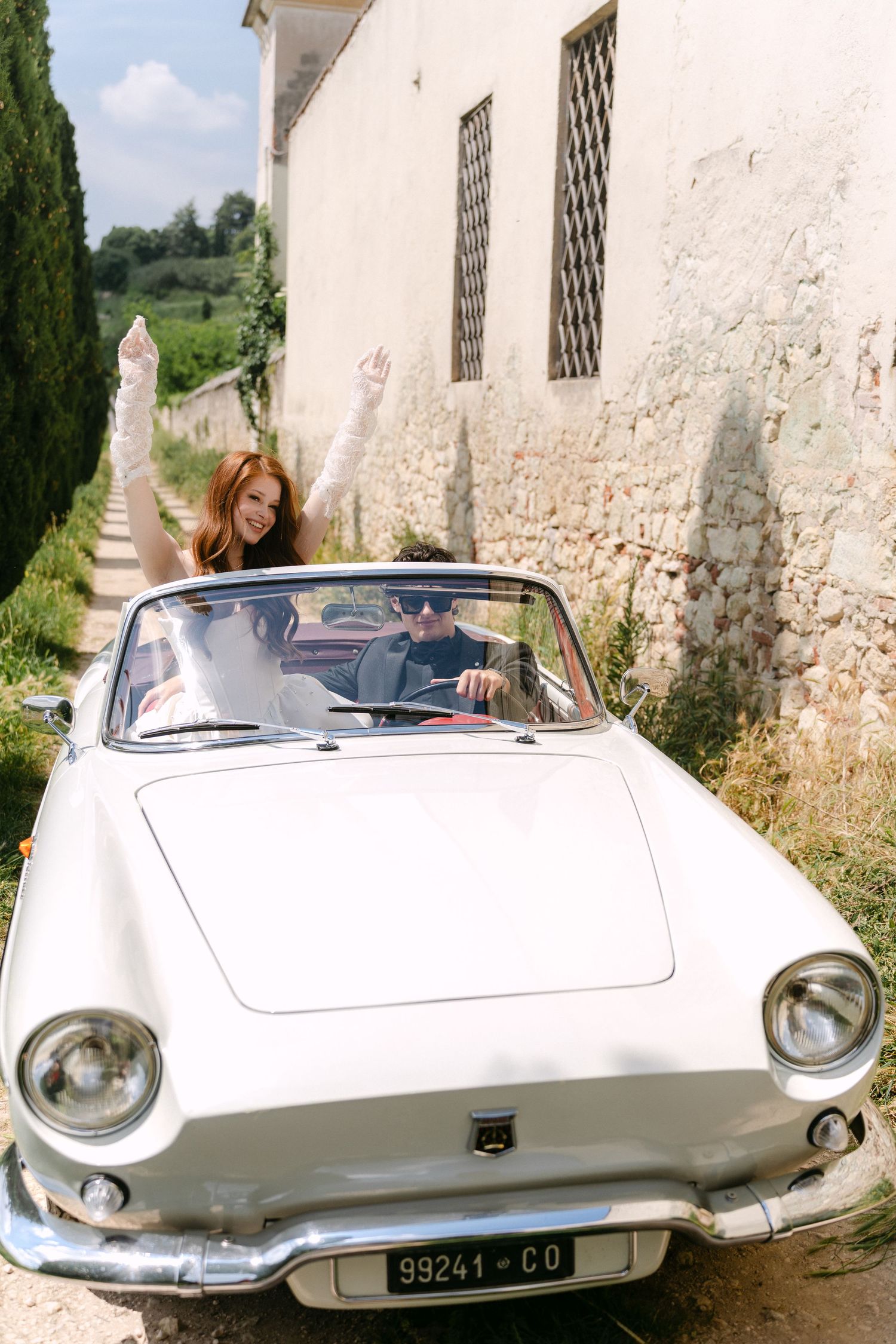 Classic white vintage convertible car parked against rustic stone wall in Italian countryside setting.