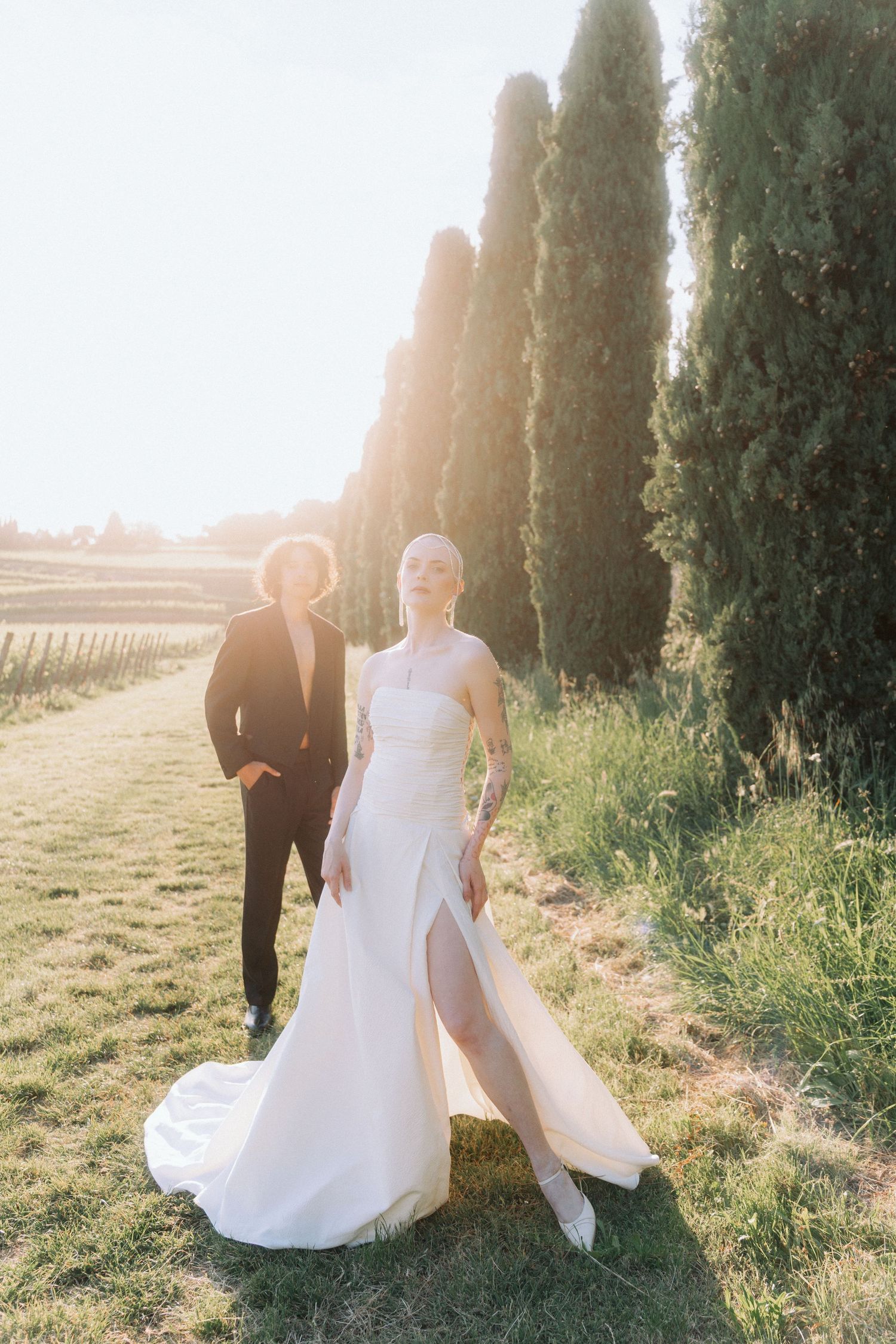 Newlywed couple walking along a cypress tree-lined path at sunset in Tuscany during golden hour.
