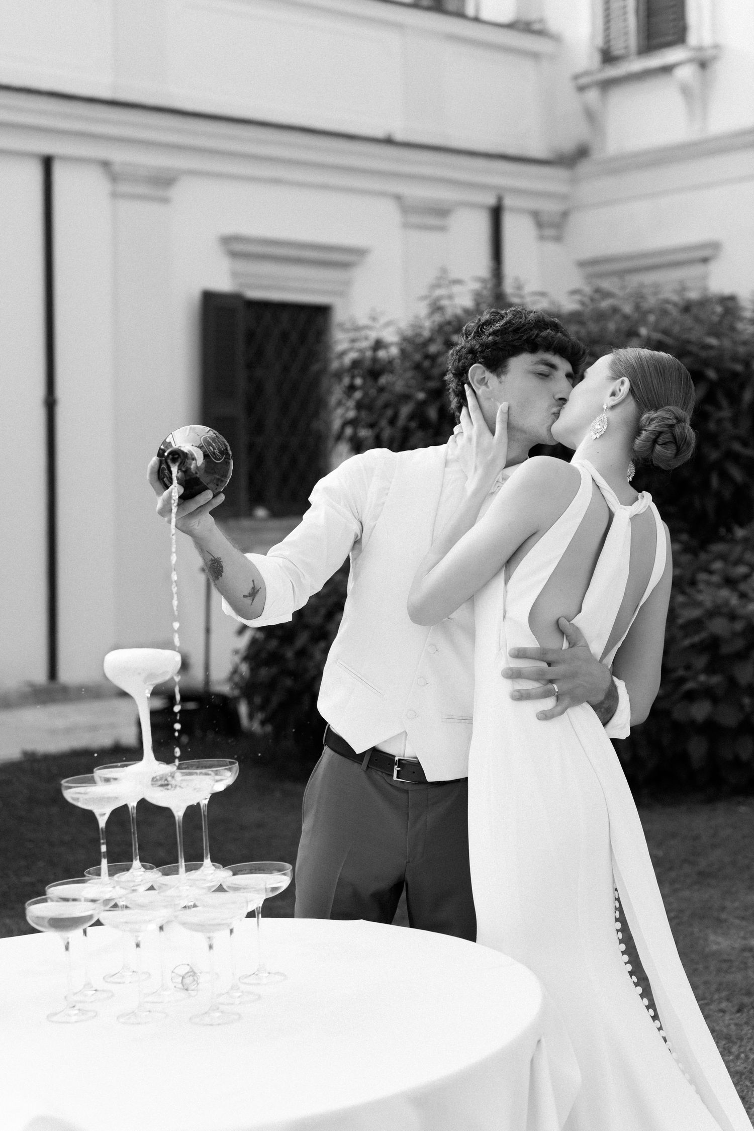 A romantic black and white photo series of a couple sharing champagne and kissing at an elegant outdoor venue. Villa Mosconi Bertani