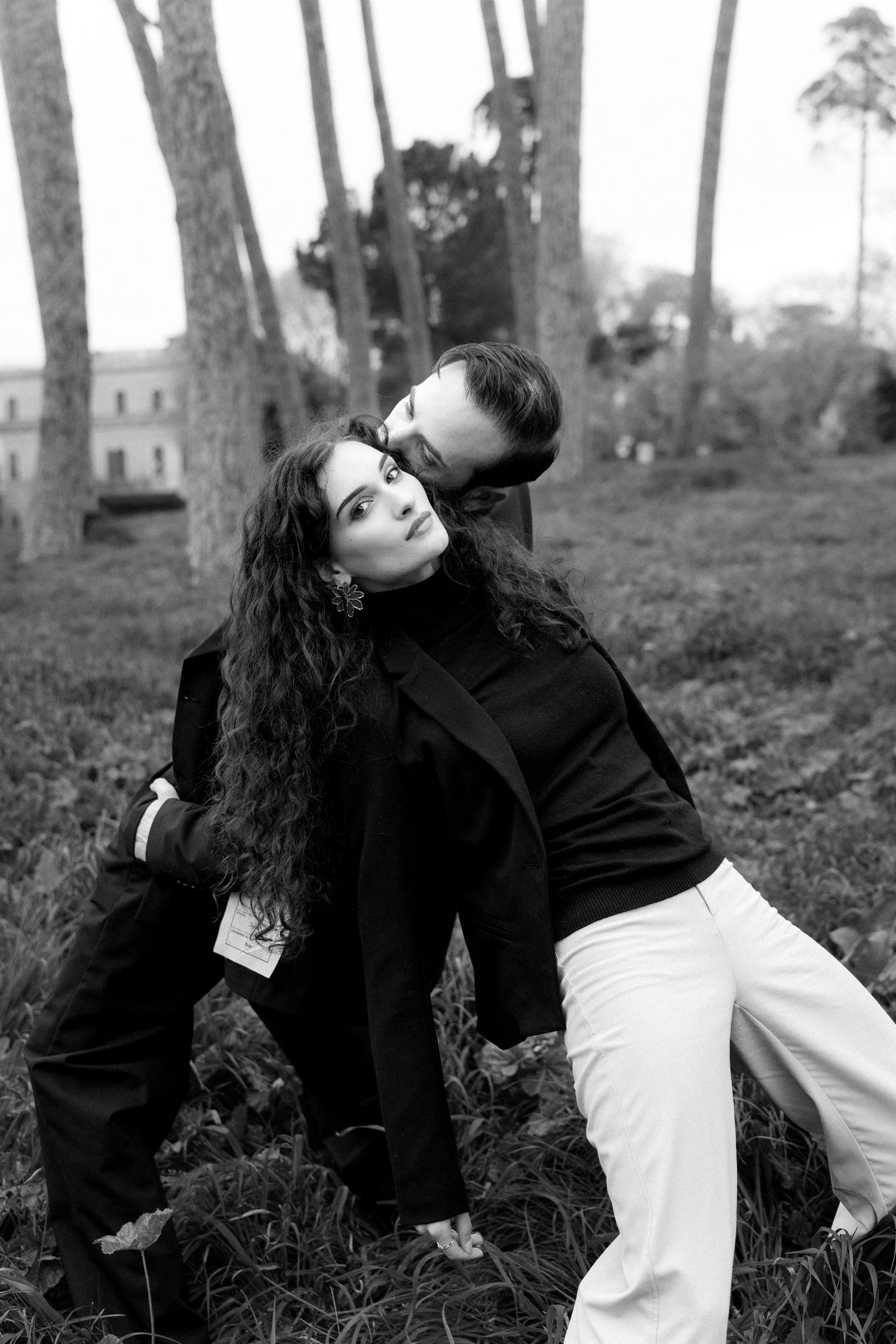 A romantic black and white photo showing a couple in contrasting black and white outfits embracing outdoors among palm trees.