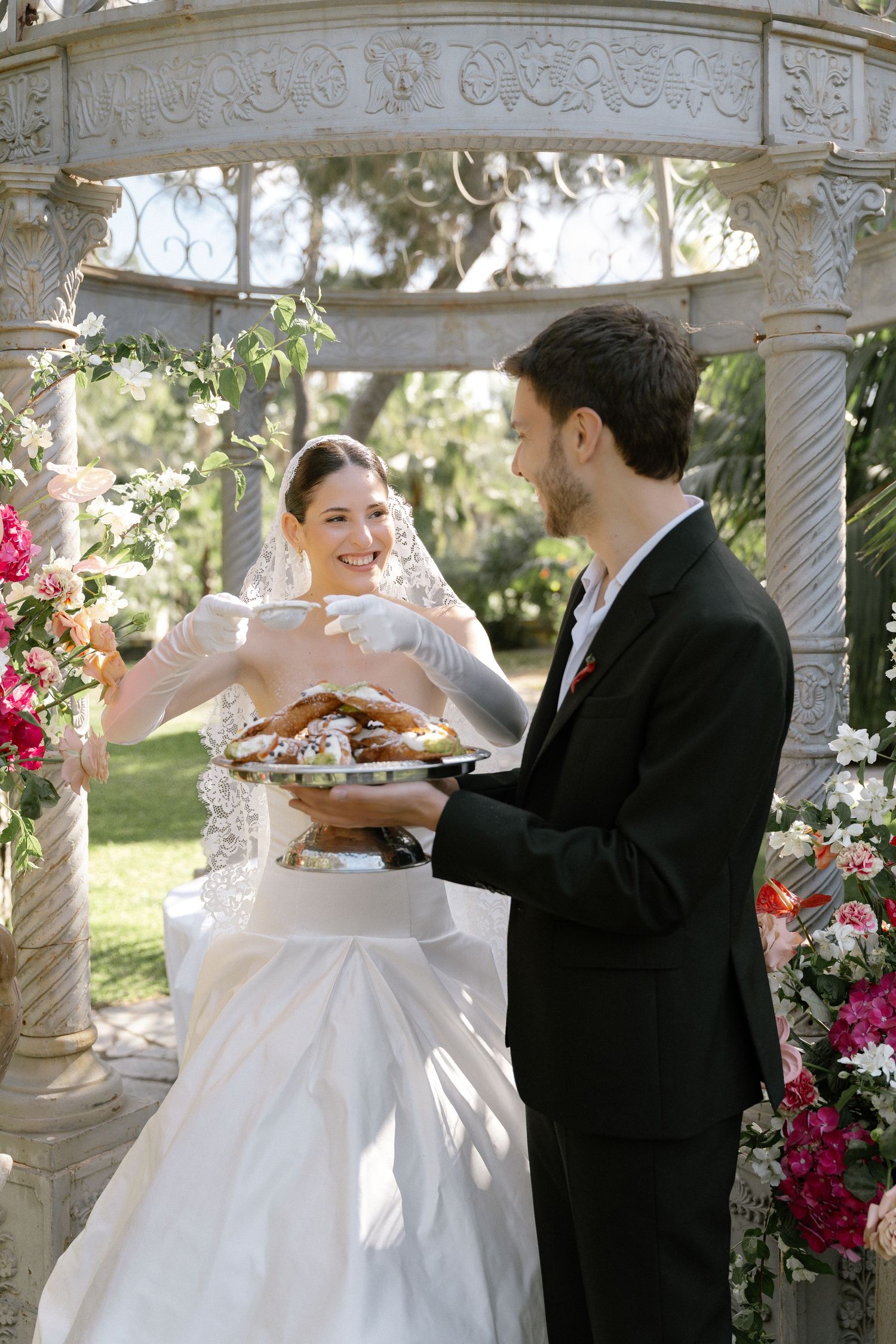 Bride and groom sharing a sweet moment under a white gazebo with floral arrangements at an outdoor wedding ceremony.