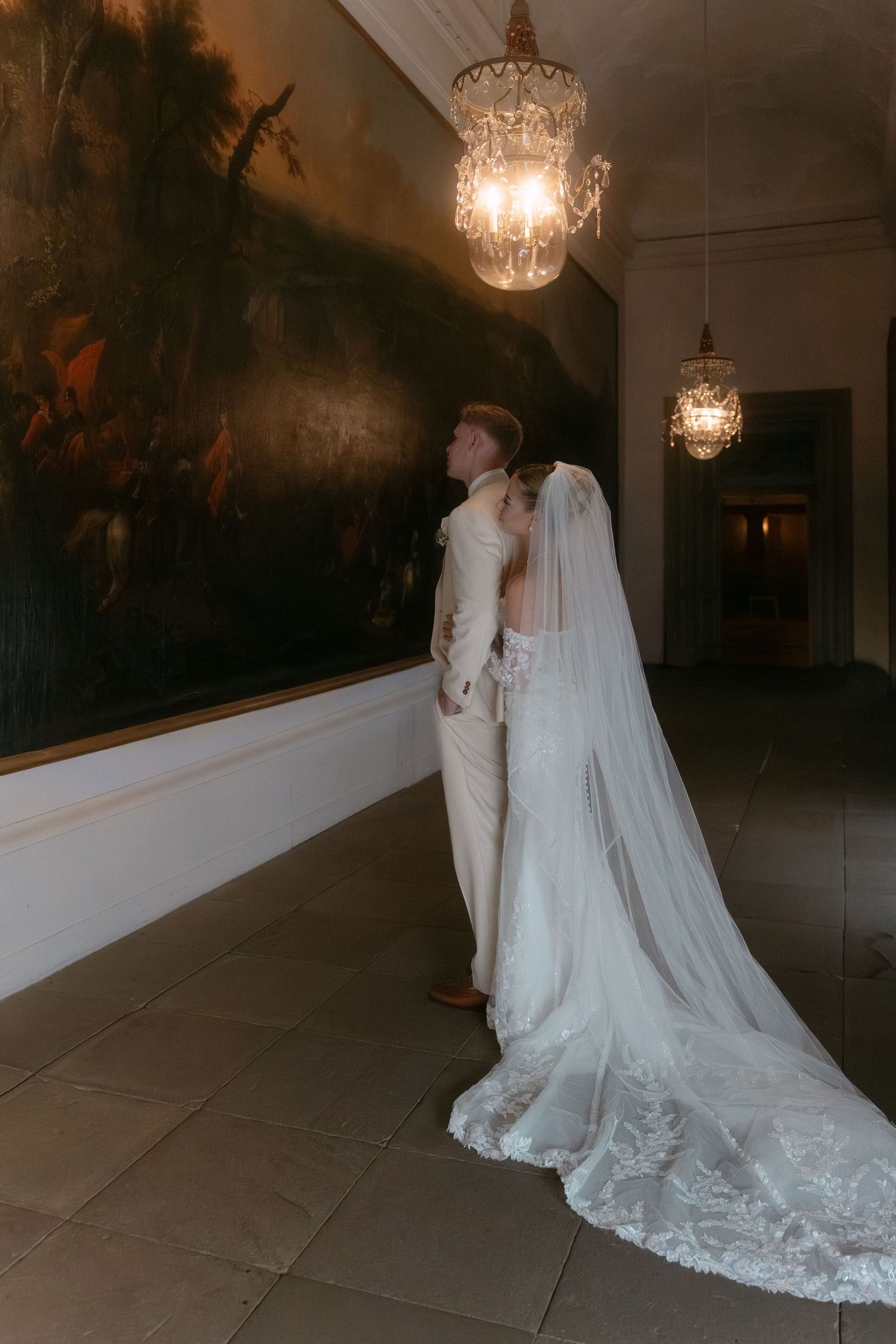 Romantic wedding photos in a dimly lit hallway with crystal chandeliers overhead.