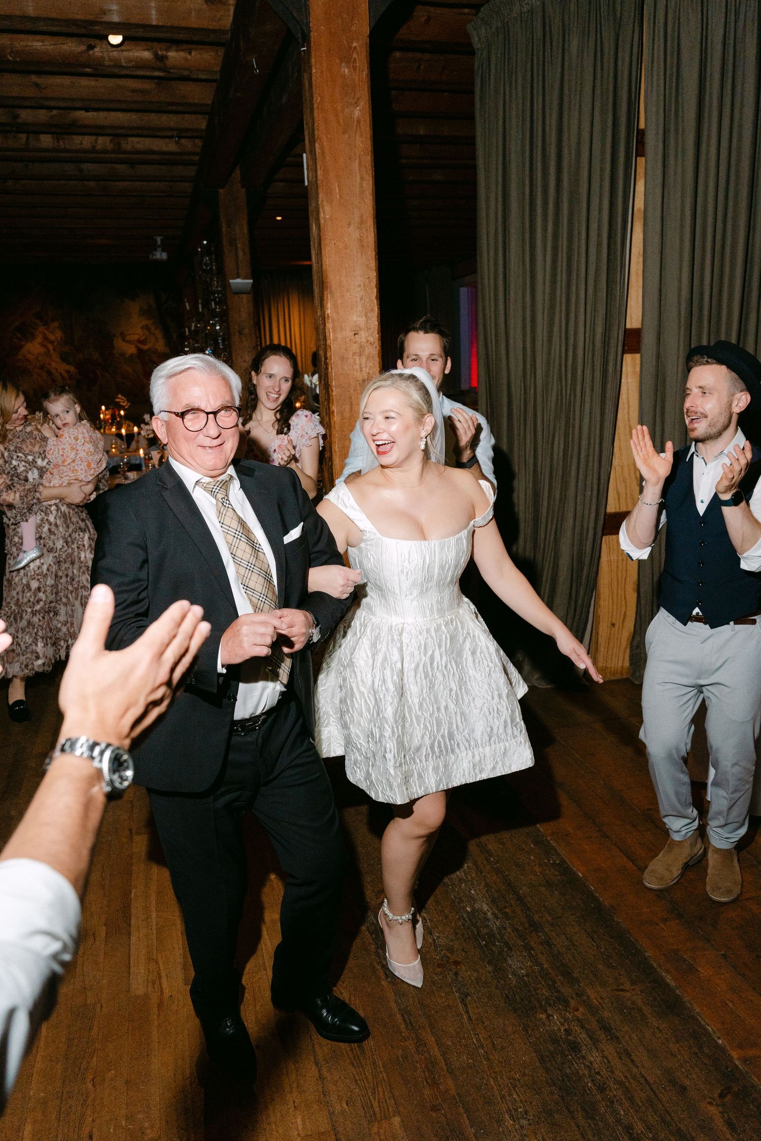 People dancing and celebrating on a wooden dance floor at what appears to be a wedding reception or party.