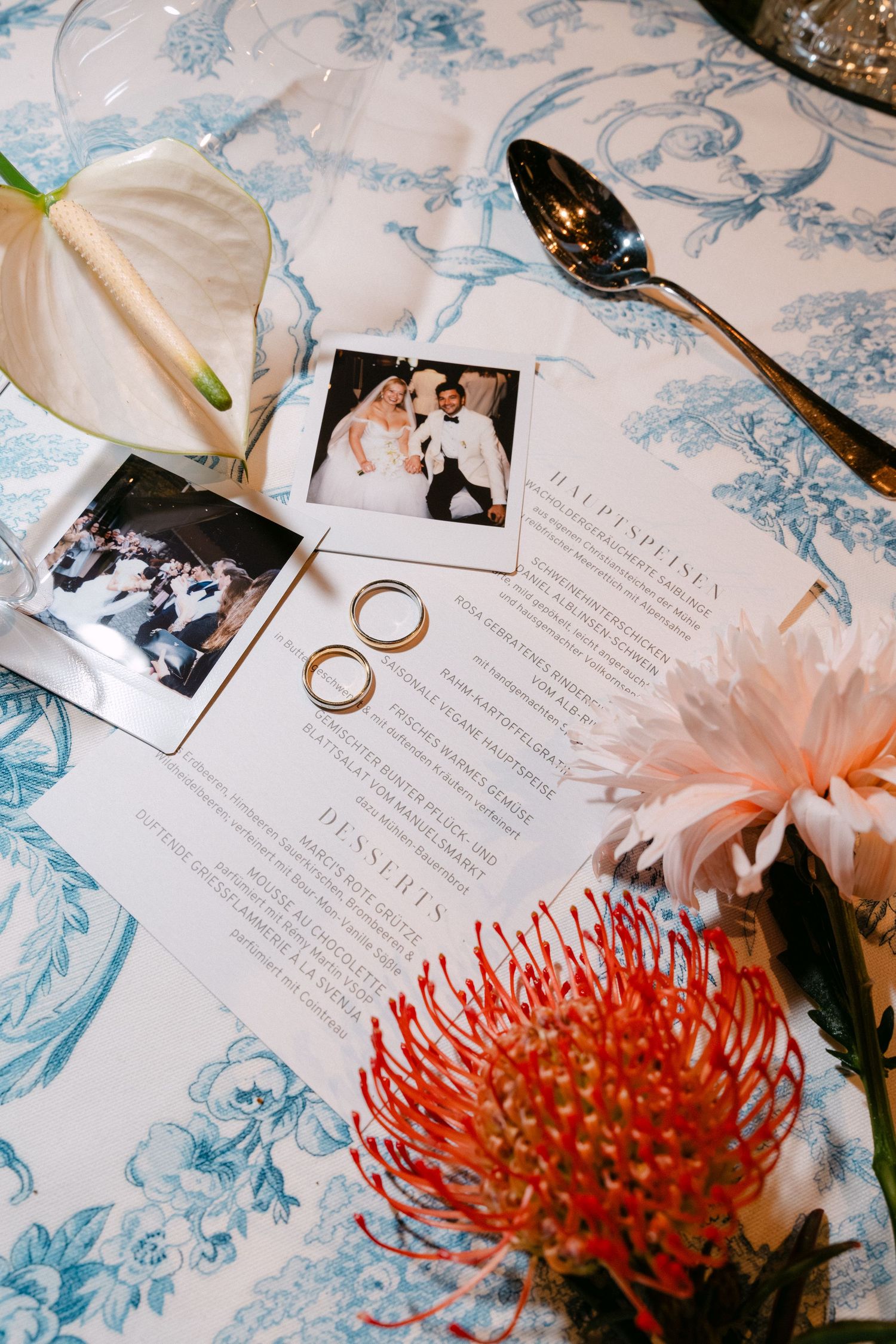 Wedding invitation details with gold rings and vibrant red protea flowers on blue and white floral background.