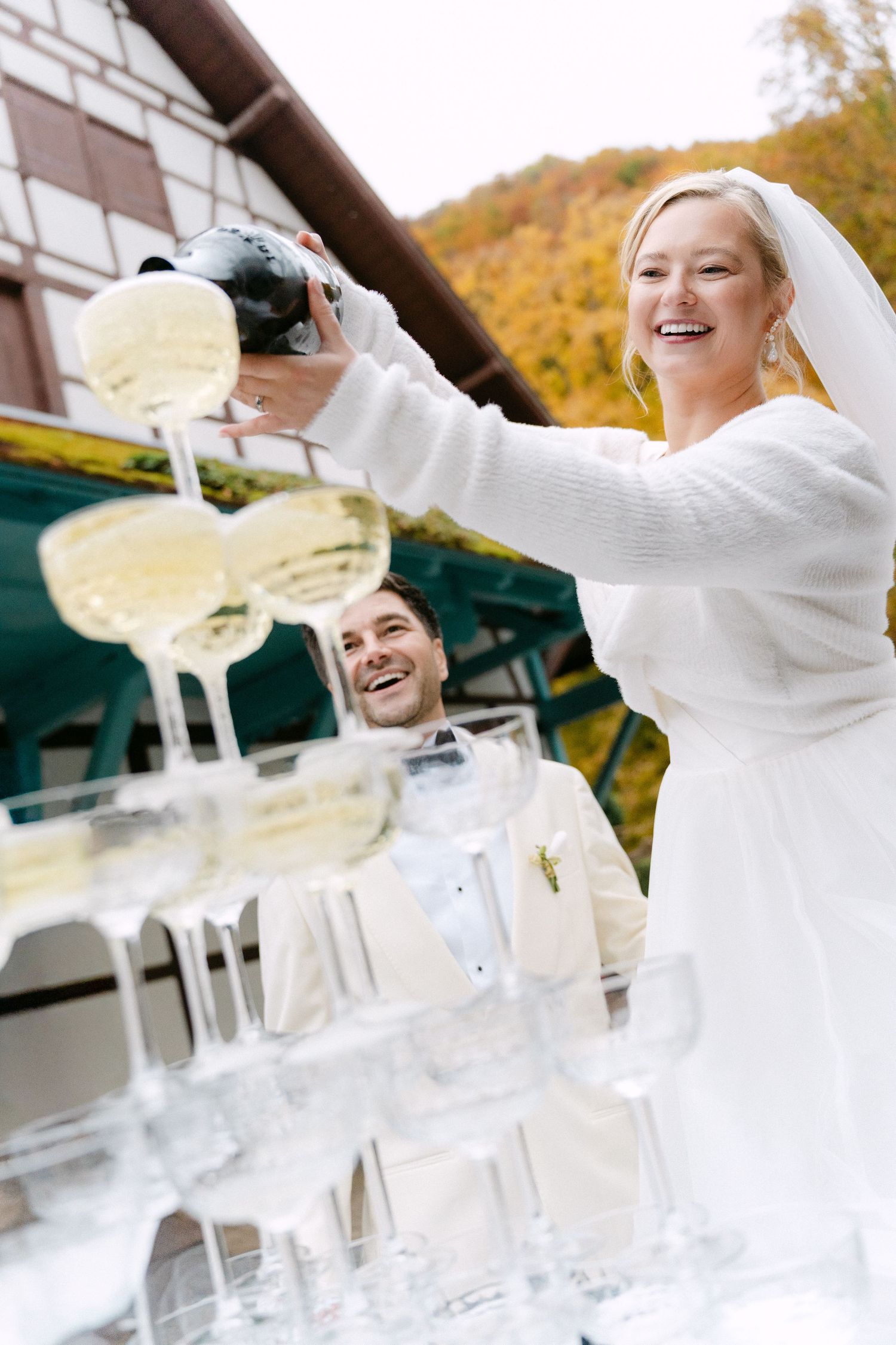 Wedding guests toss white napkins in celebration at an outdoor reception venue with autumn foliage in background.