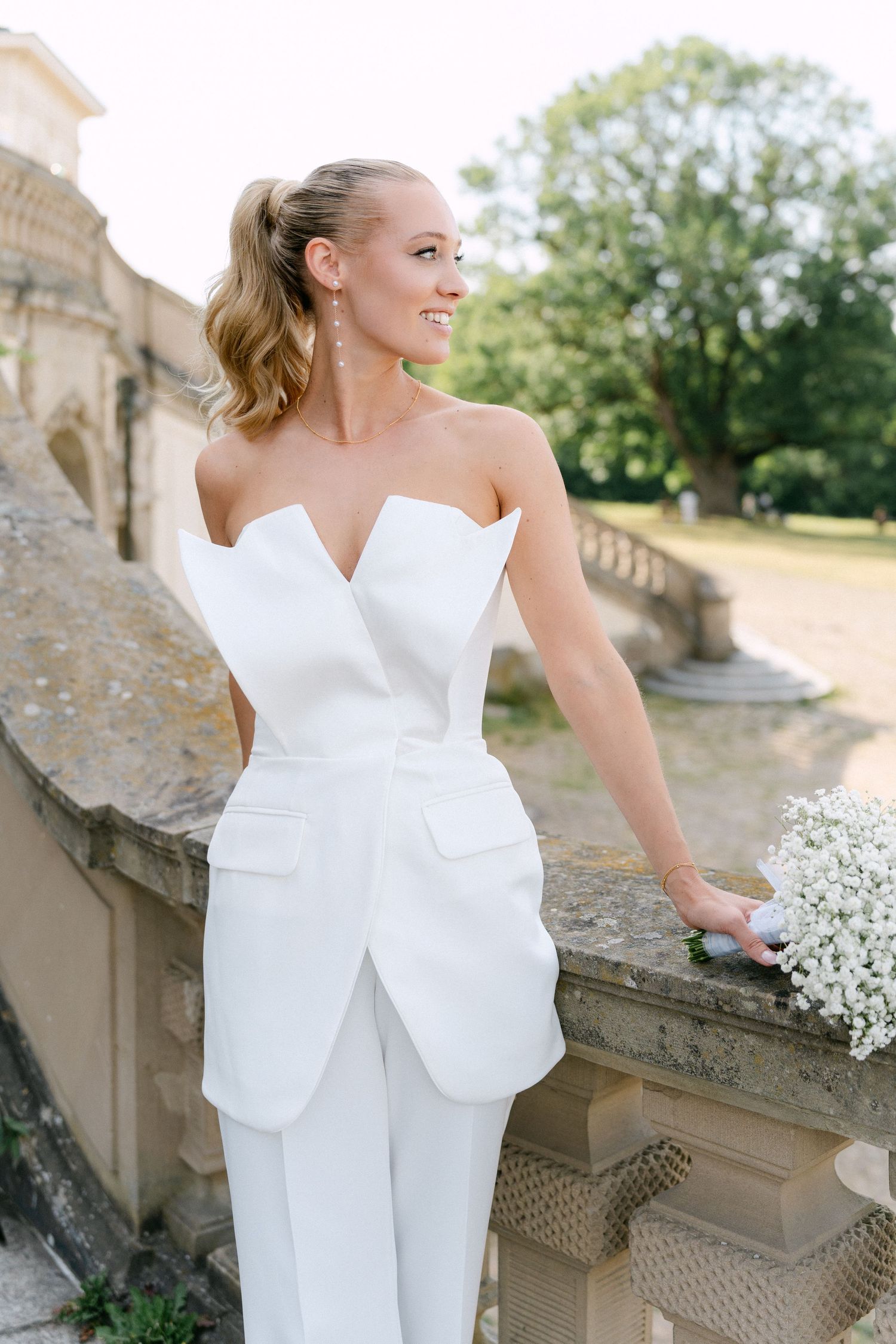 Modern bridal jumpsuit with strapless sweetheart neckline and architectural details photographed at historic stone venue. Schloss Solitude