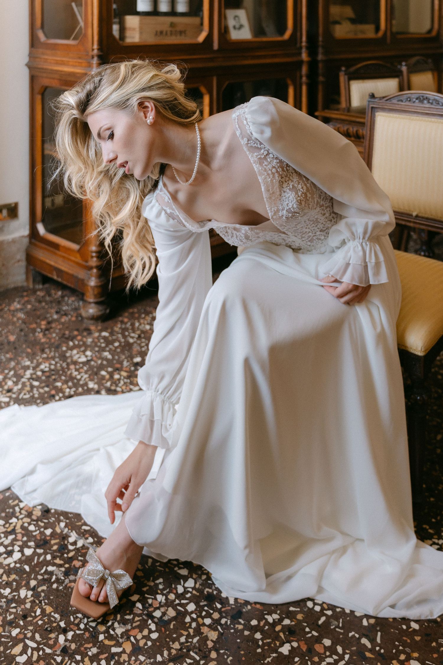 A person in a flowing white dress sits gracefully on a patterned floor in an elegant vintage-style interior. Wedding Verona